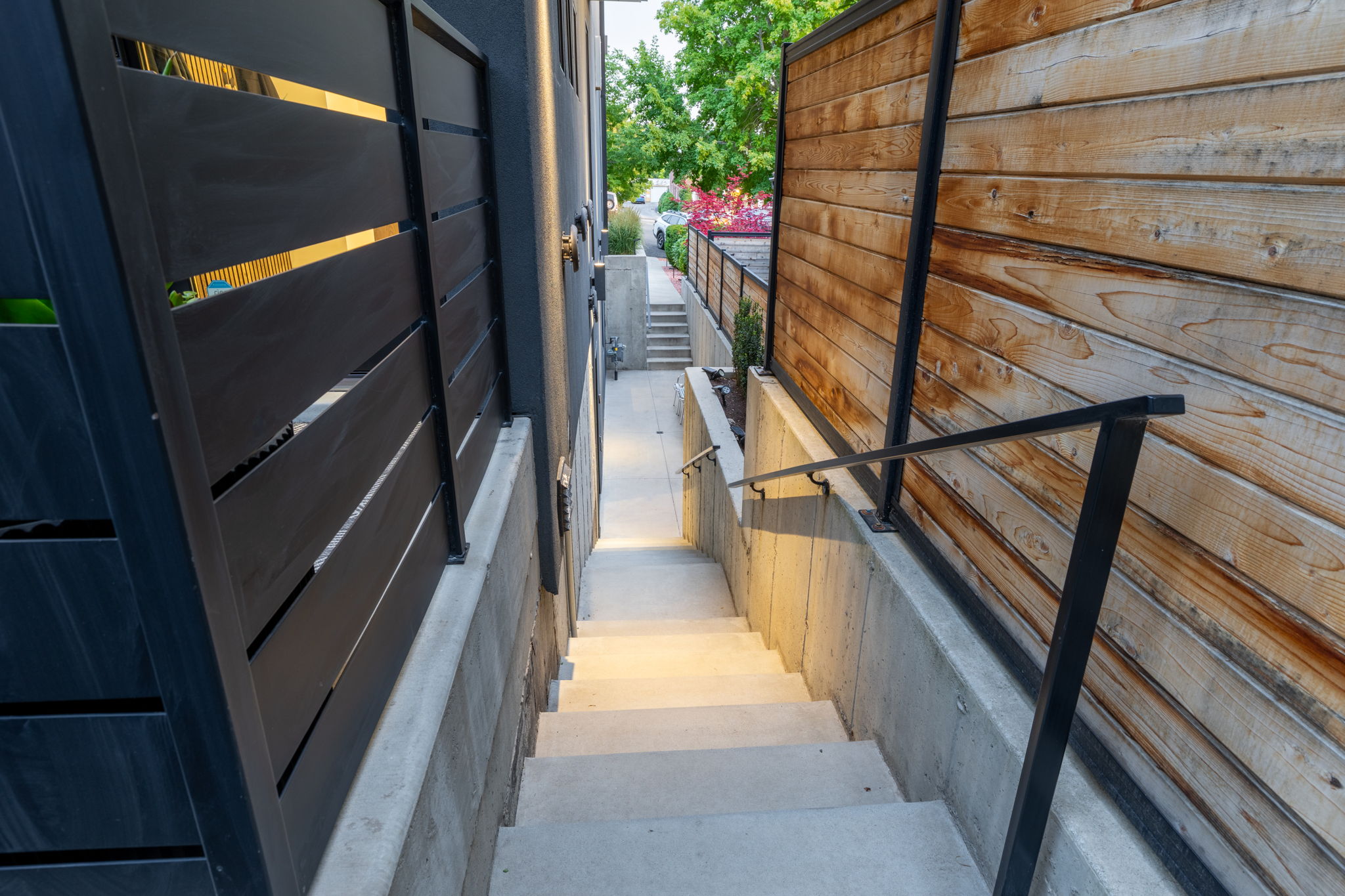 Concrete stairway with integrated wall lighting, black metal handrails, and a slatted wood privacy fence