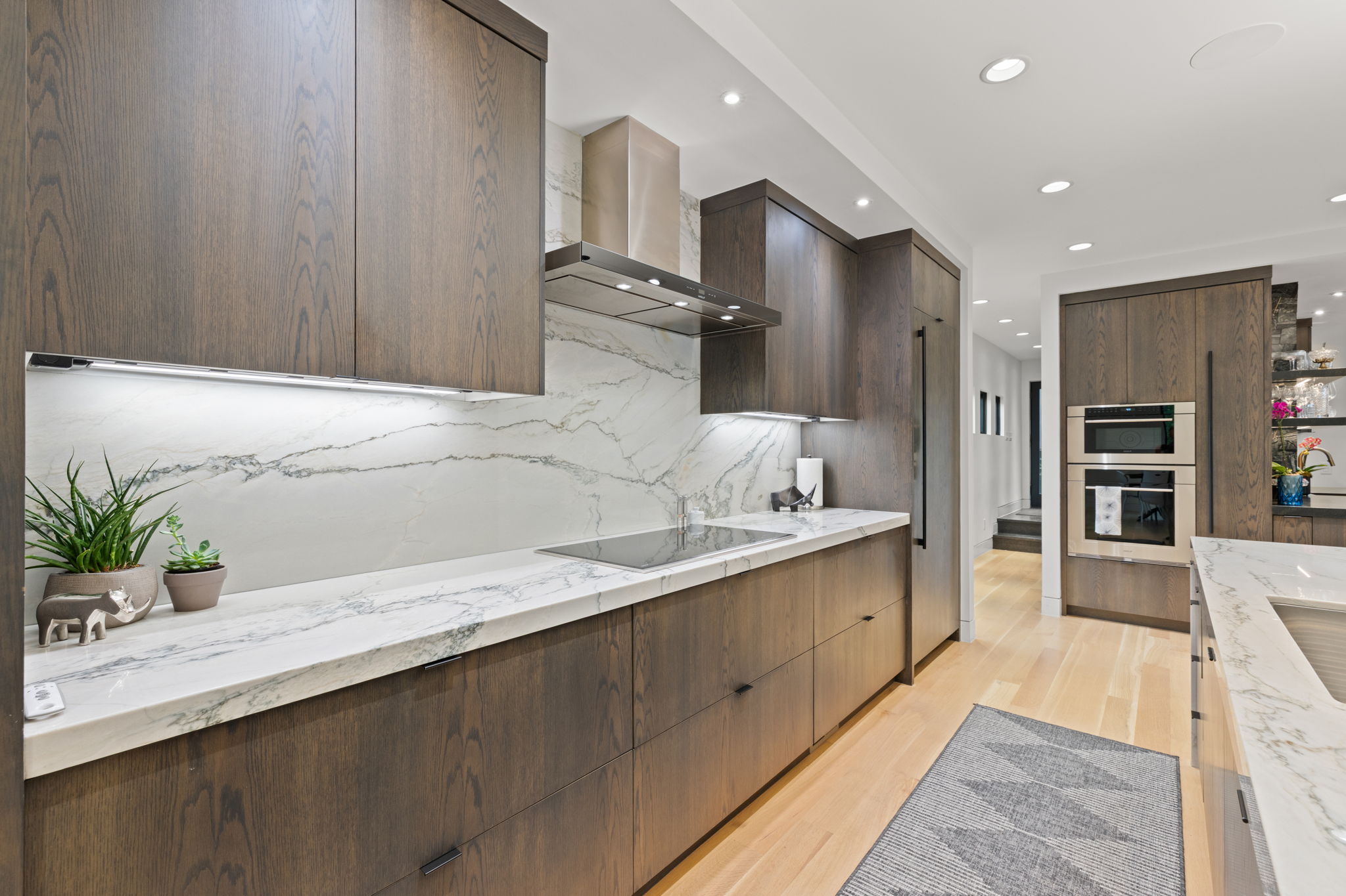 Contemporary kitchen featuring dark wood-finish cabinetry, light wood-finish flooring, and white countertops with a patterned veining