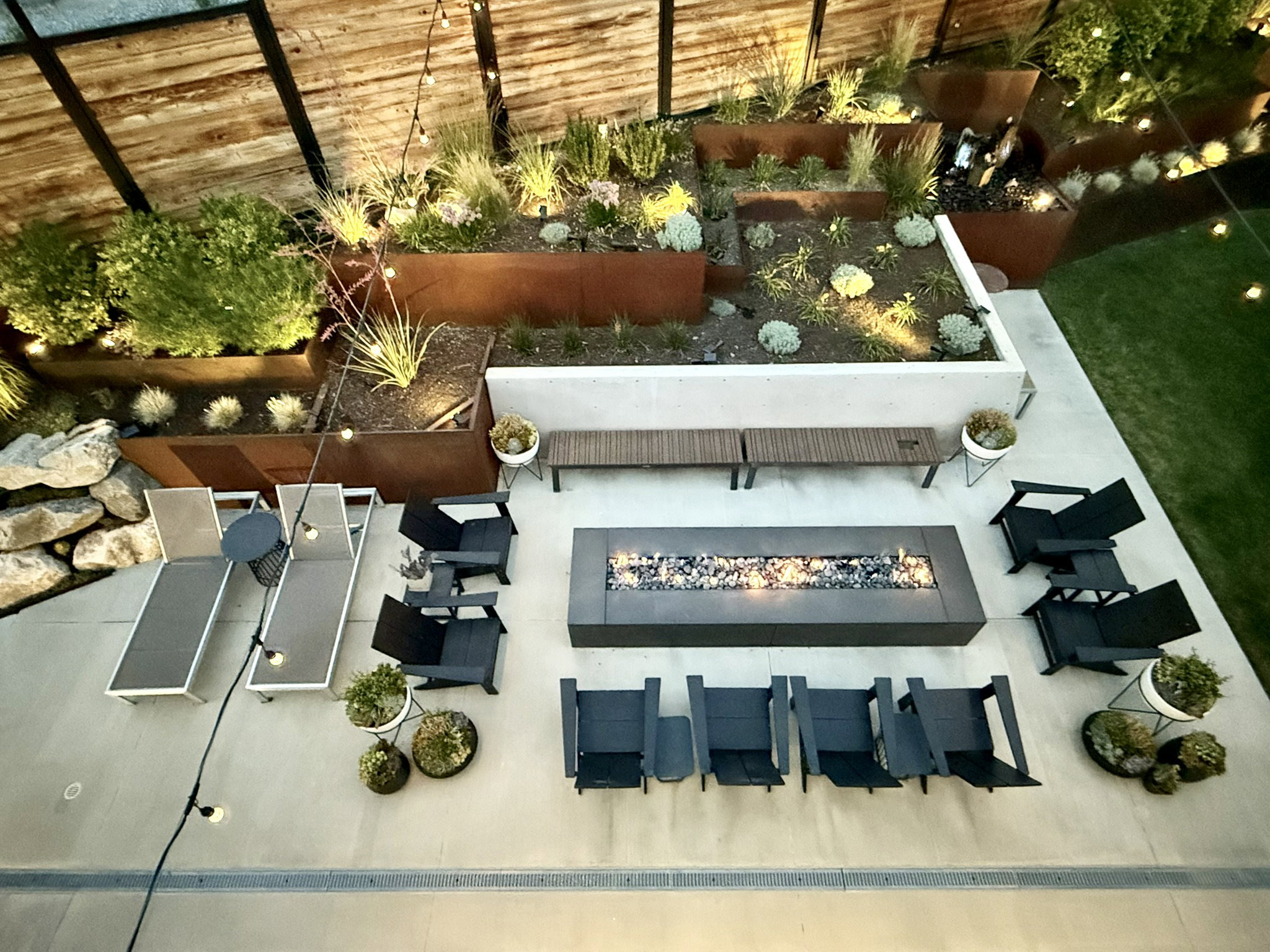 Outdoor living area featuring a rectangular fire pit with stone accents, a concrete patio, and tiered landscaping with integrated lighting