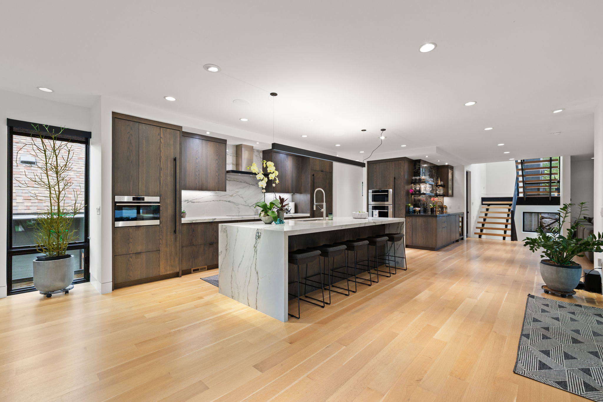 Open-concept kitchen featuring an oversized island with waterfall-edge countertop, integrated appliances, recessed lighting, and light wood-finish flooring