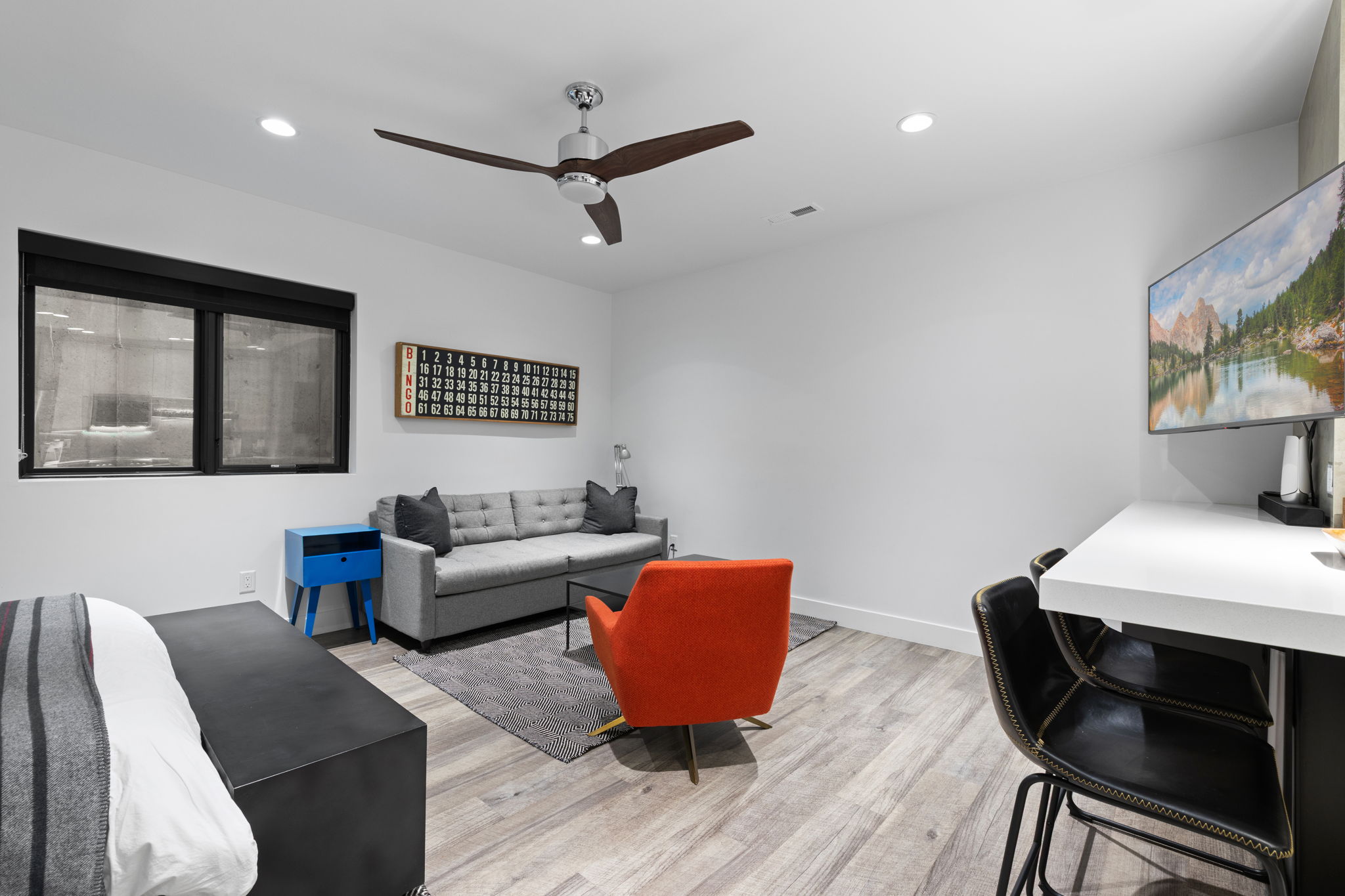Bright interior space featuring wood-finish flooring, a contemporary ceiling fan, recessed lighting, a built-in countertop, and a window with a roller shade