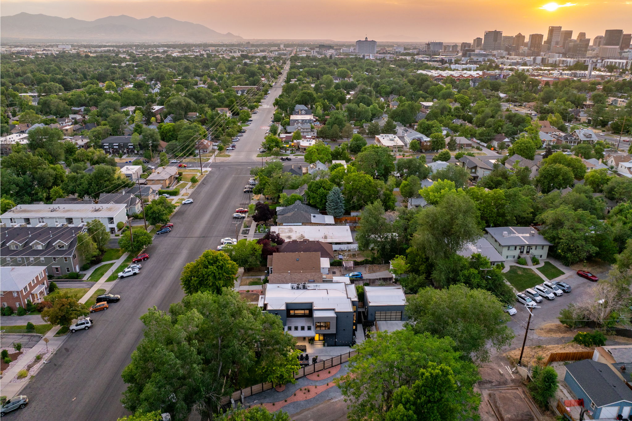 Aerial perspective showcasing an urban neighborhood with a prominent cityscape and distant mountains under a dramatic sky