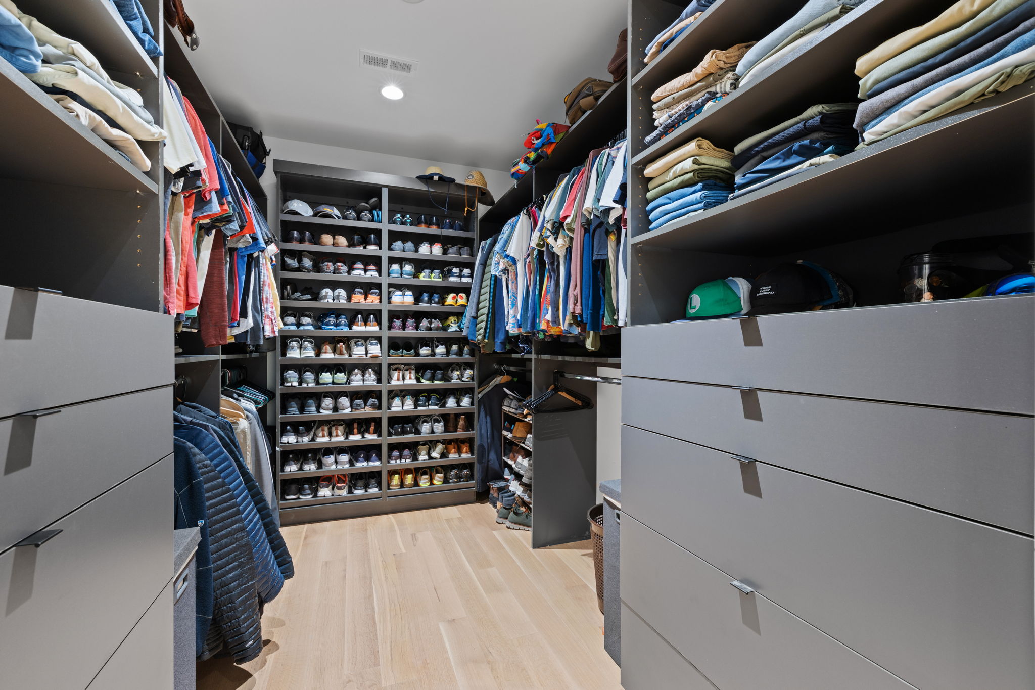 Custom closet system featuring light wood-finish flooring, recessed lighting, integrated shelving, and multiple built-in drawers