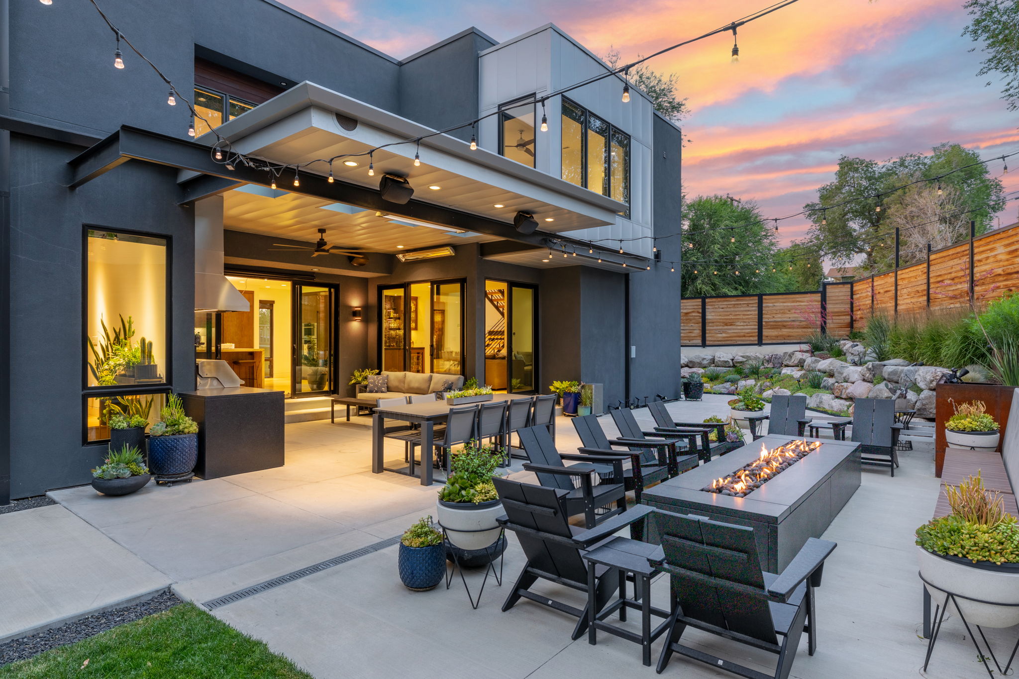 Spacious outdoor patio with an integrated fire pit, covered dining area, built-in grill station with a range hood, string lighting, and extensive concrete hardscaping