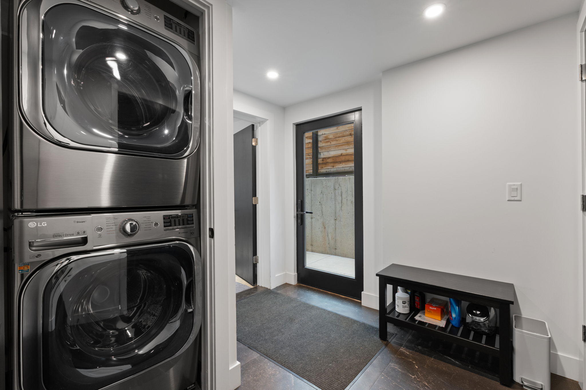 Dedicated laundry area featuring a stacked washer and dryer, recessed lighting, white walls, and dark flooring