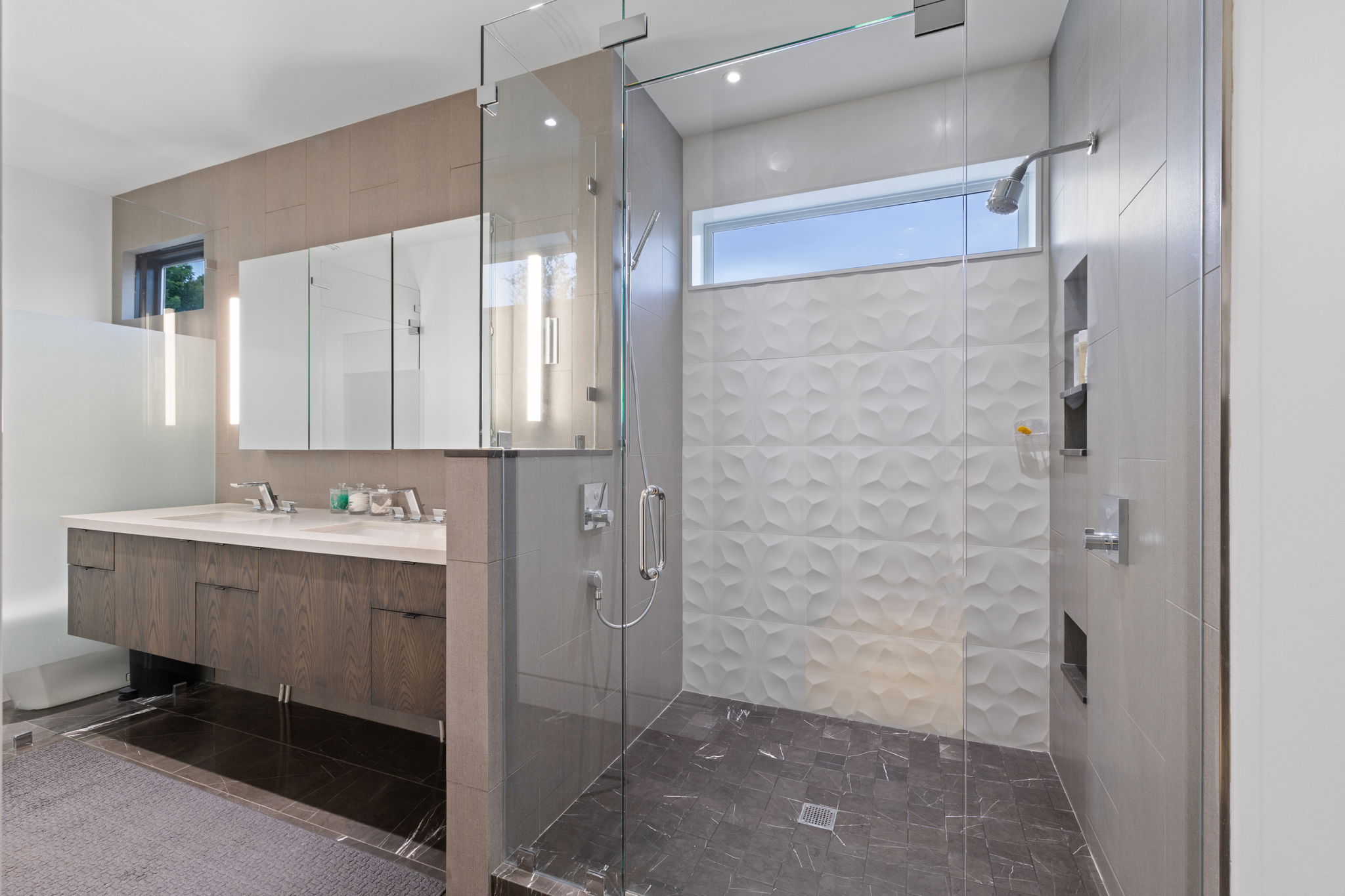 Spacious walk-in shower with a textured accent wall, integrated niche shelving, and a transom window
