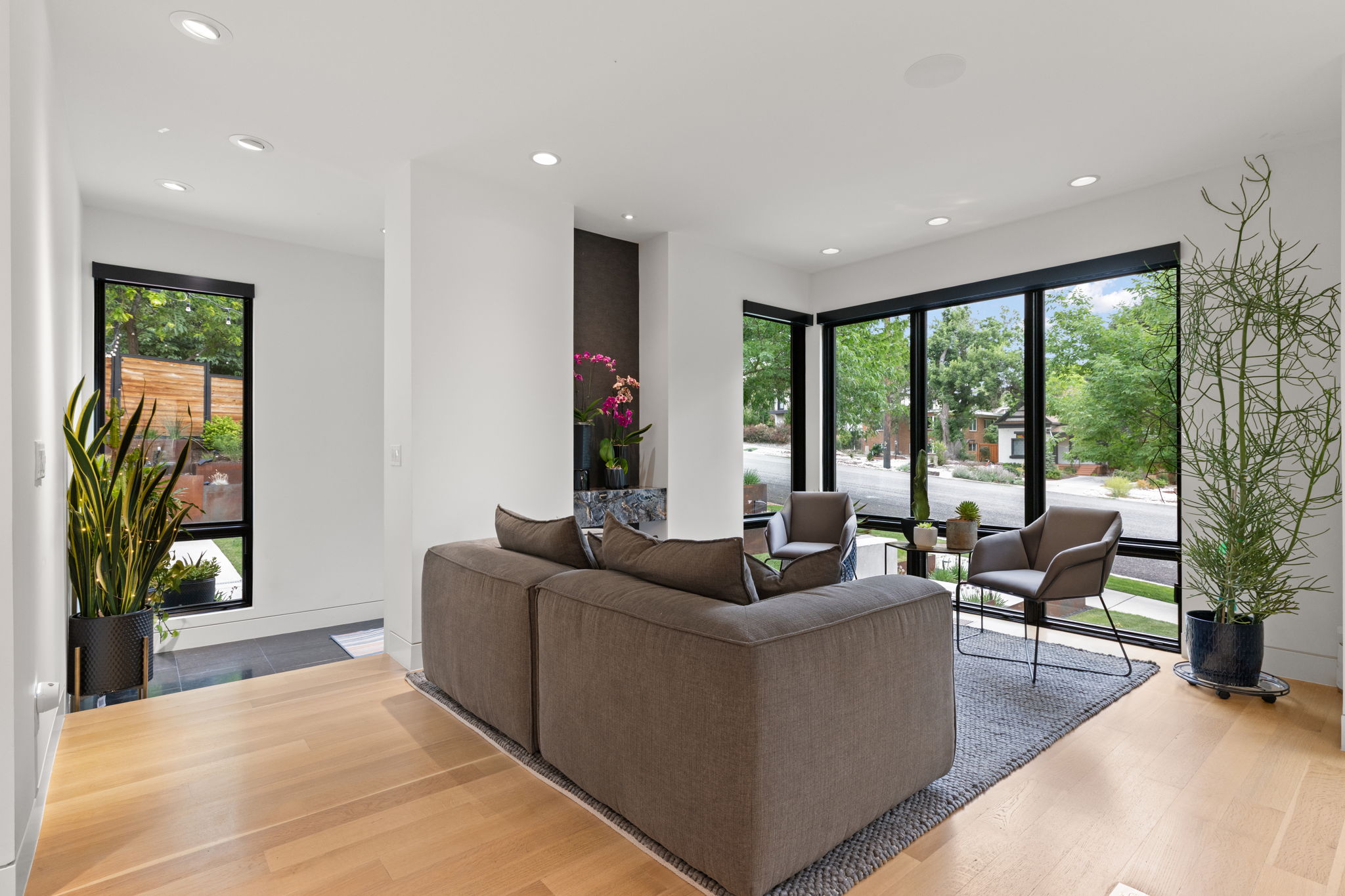 Living space featuring expansive black-framed windows, light wood-finish flooring, recessed lighting, and a dark accent wall with a stone-finish ledge