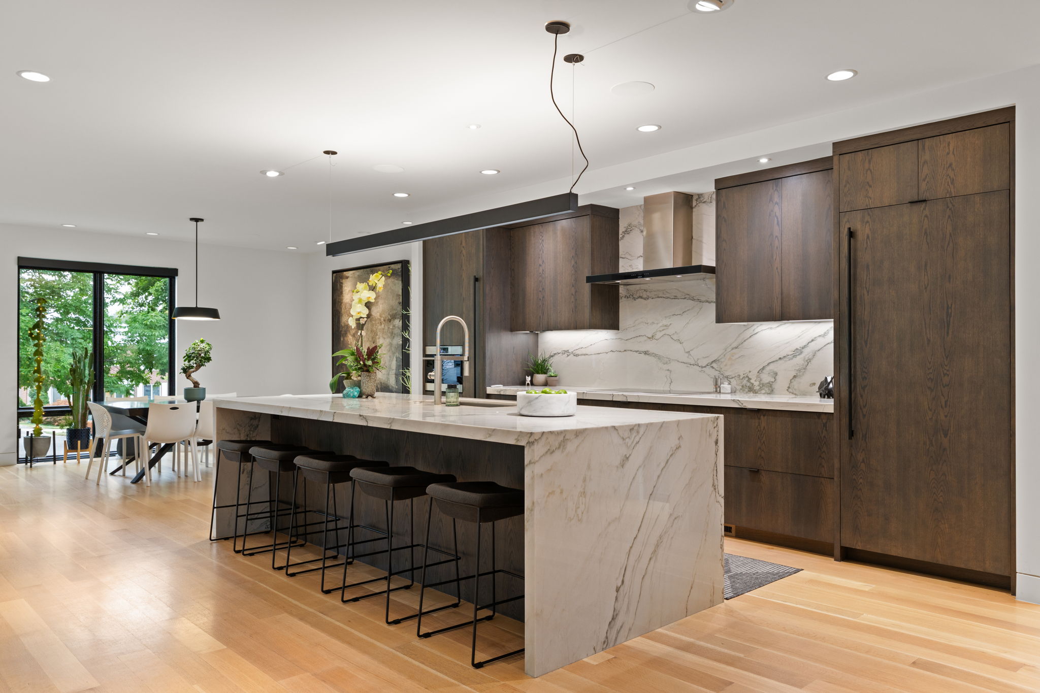 Gourmet kitchen featuring a waterfall island, integrated appliances, wood-finish cabinetry, and marble-look slab backsplash
