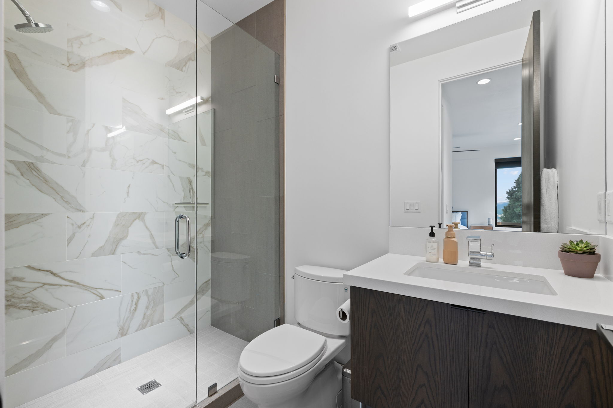 Contemporary bathroom featuring a glass-enclosed shower with large format marbled tile, a dark wood-finish vanity, and a rectangular undermount sink with a chrome faucet