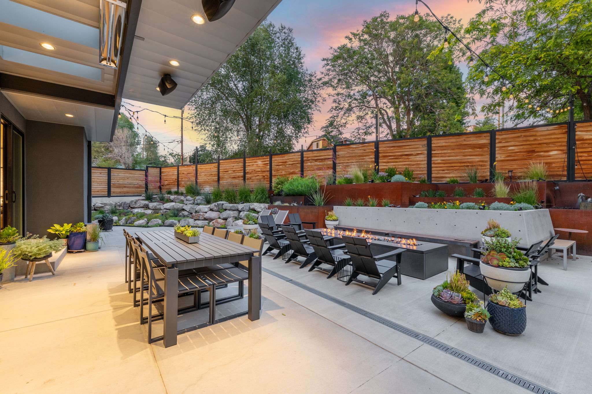 Expansive outdoor living area featuring a concrete patio, built-in fire pit, and a tiered landscaped garden with a wooden privacy fence