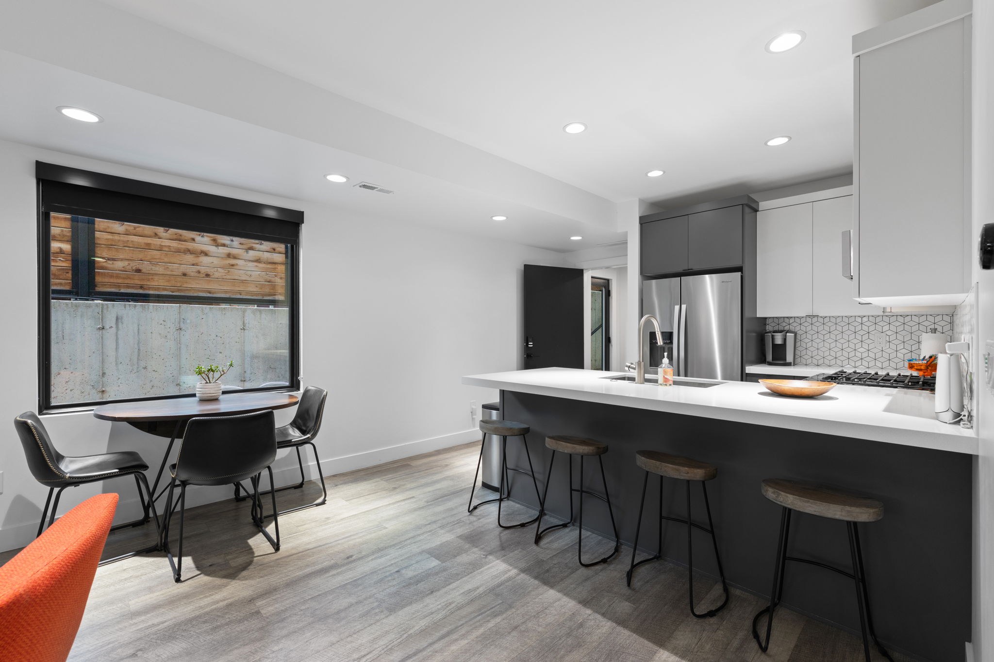 Modern kitchen featuring two-tone cabinetry, stainless steel refrigerator, hexagonal tile backsplash, and an island with bar seating