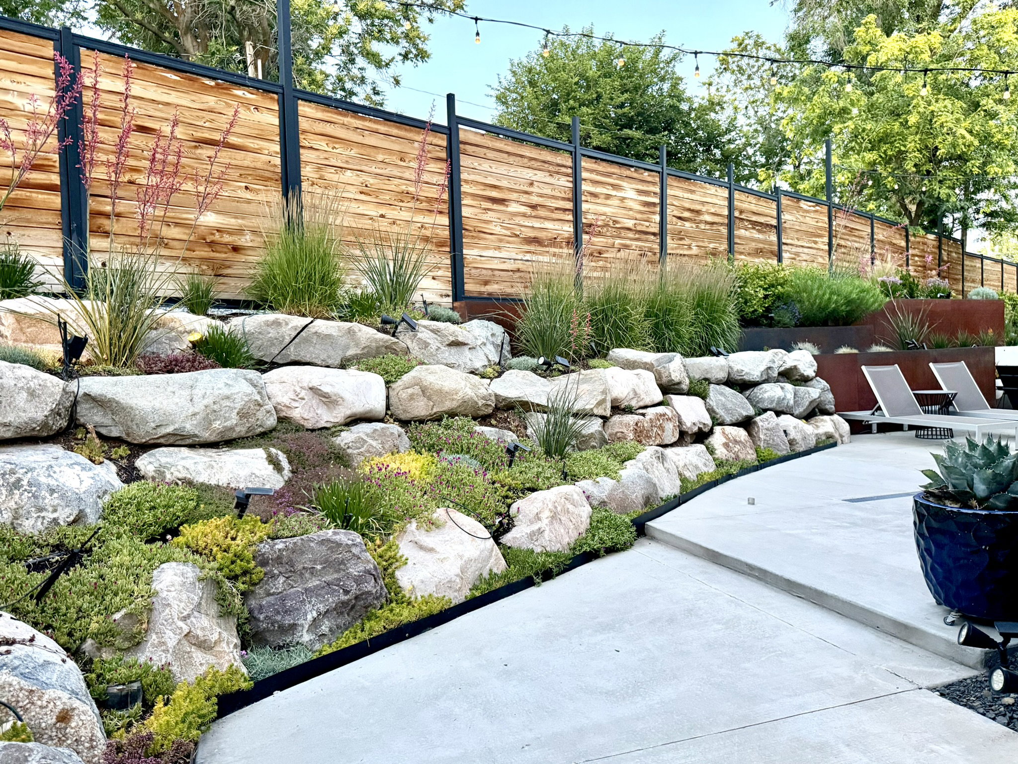 Stone retaining wall with integrated plantings, complemented by a horizontal wood and metal privacy fence