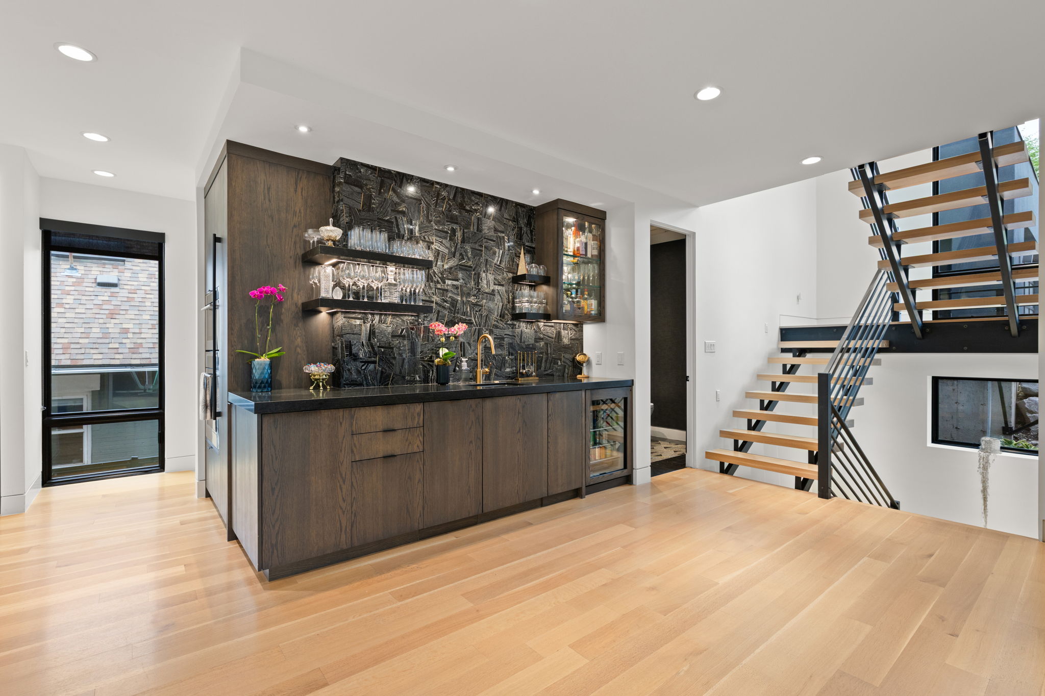 Contemporary open-concept space featuring a built-in wet bar with dark wood cabinetry, a textured stone backsplash, and an integrated beverage refrigerator