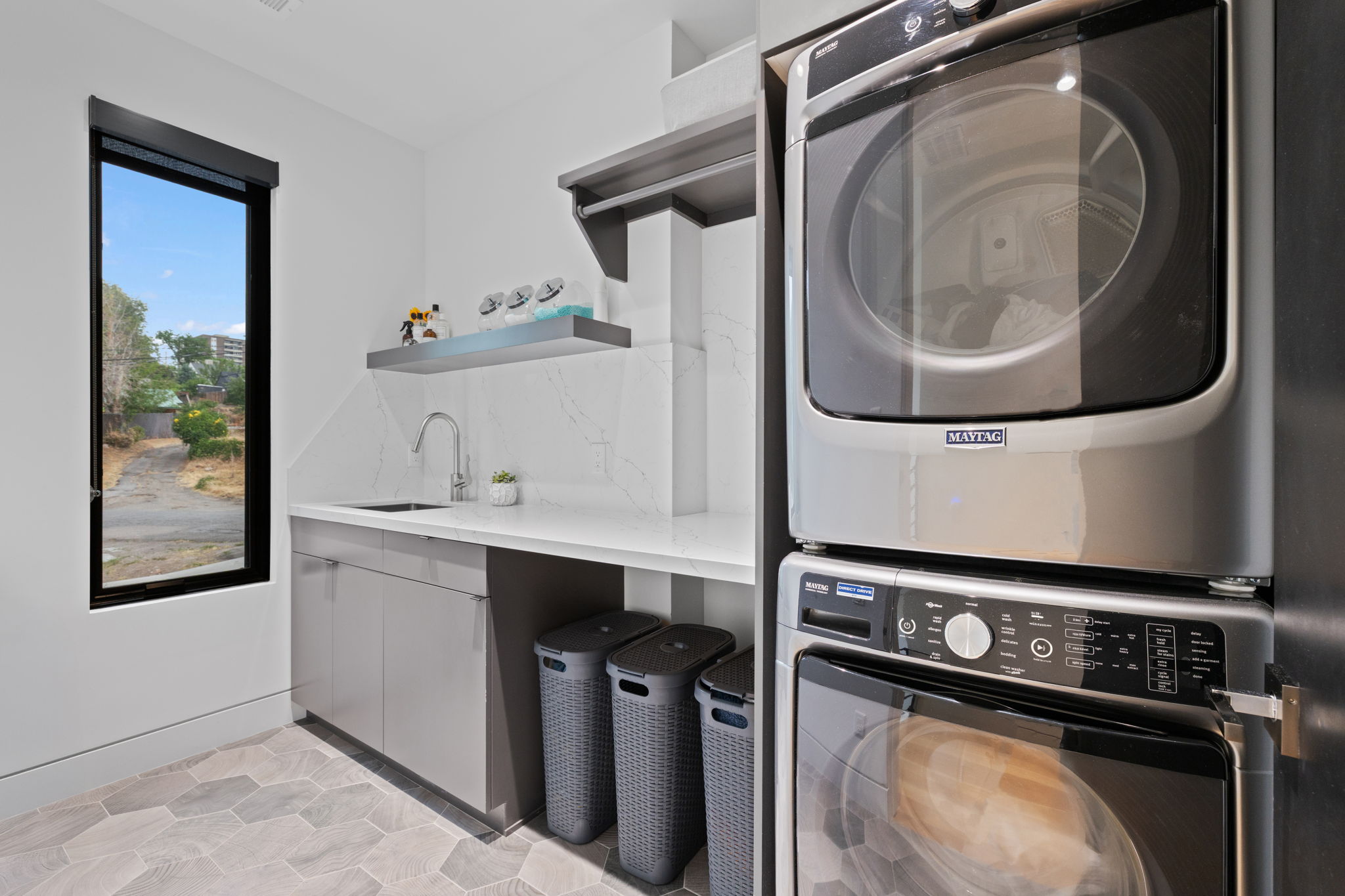 Laundry area featuring a stacked washer and dryer, hexagon tile flooring, white countertops, a sink with a gooseneck faucet, and a large window