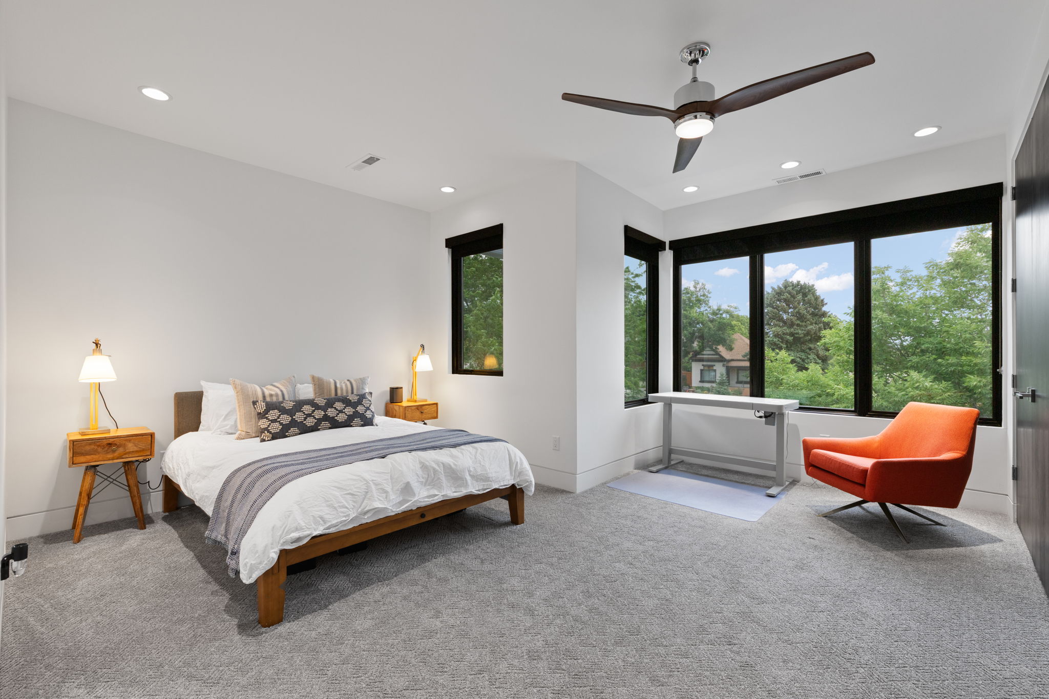Carpeted room featuring a ceiling fan with integrated lighting, multiple recessed lights, a wall of large windows, and a dark wood-finish door