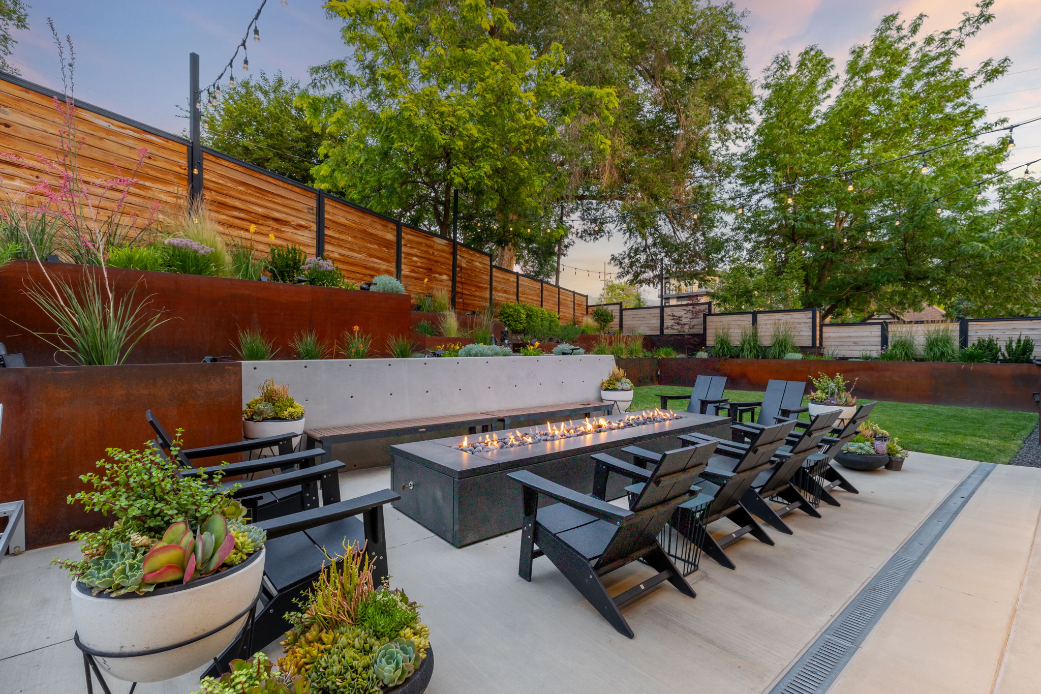 Outdoor patio featuring a linear fire pit, a built-in concrete bench, and multiple black Adirondack chairs