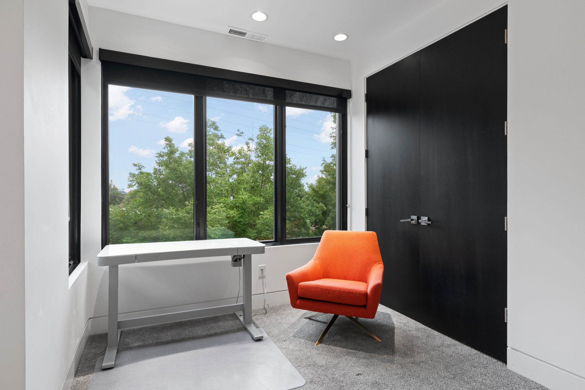 Room featuring expansive windows with black trim, recessed lighting, and a dark wood-finish door with brushed nickel hardware