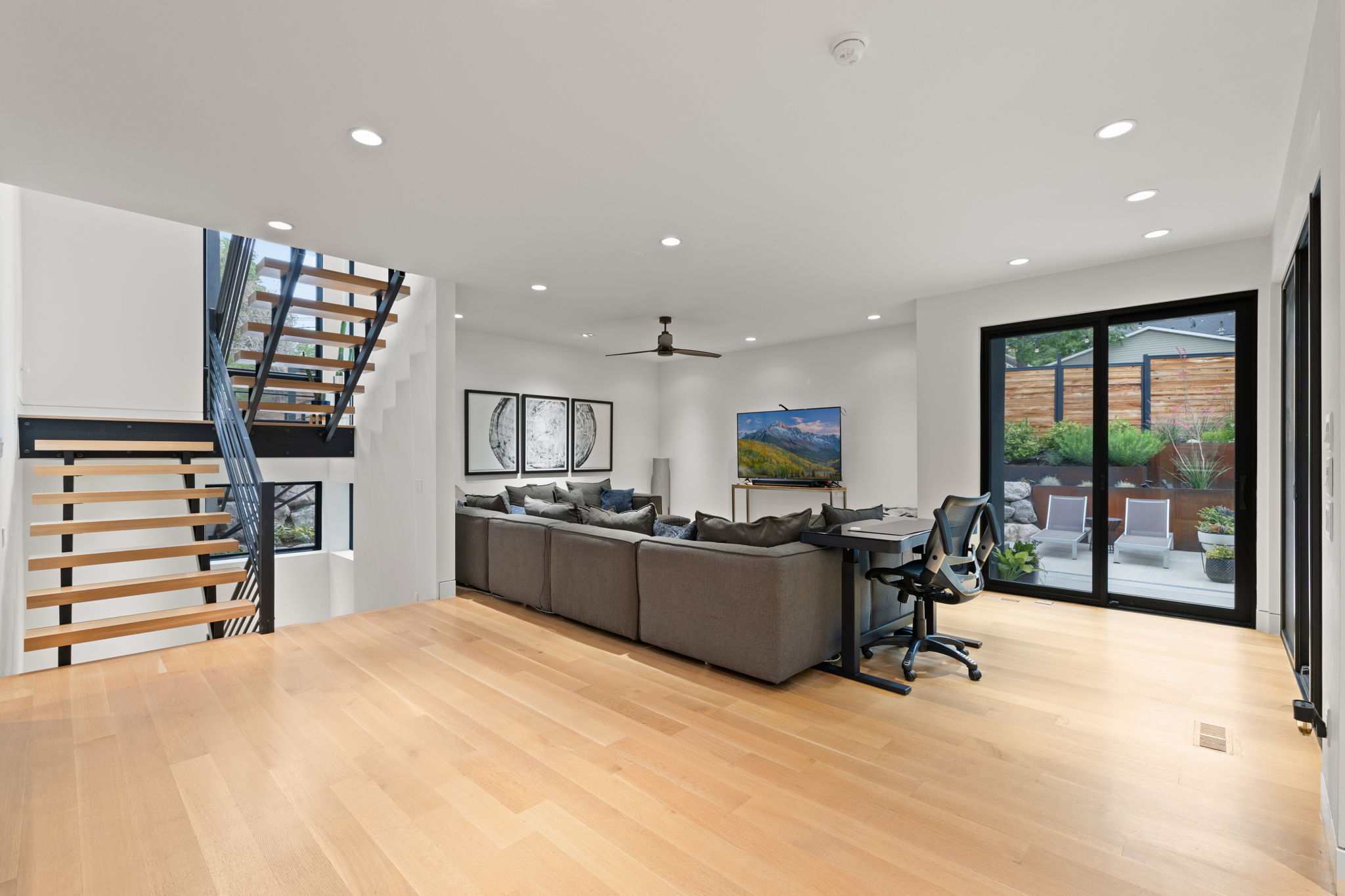 Open-concept living area with light wood-finish flooring, recessed lighting, and a contemporary open-riser staircase with black metal railings