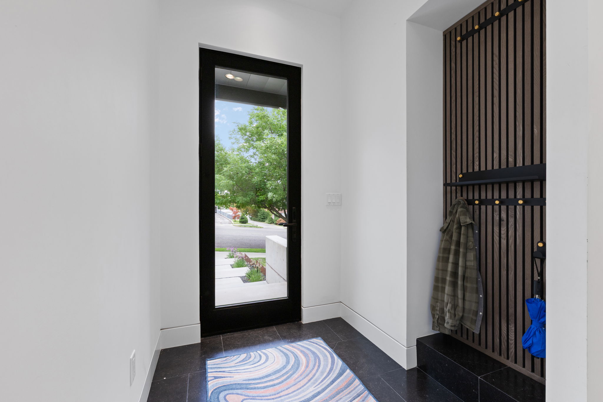 Entryway featuring a full-light door with black framing, dark tile flooring, and a built-in slatted wood panel with integrated hooks and shelving