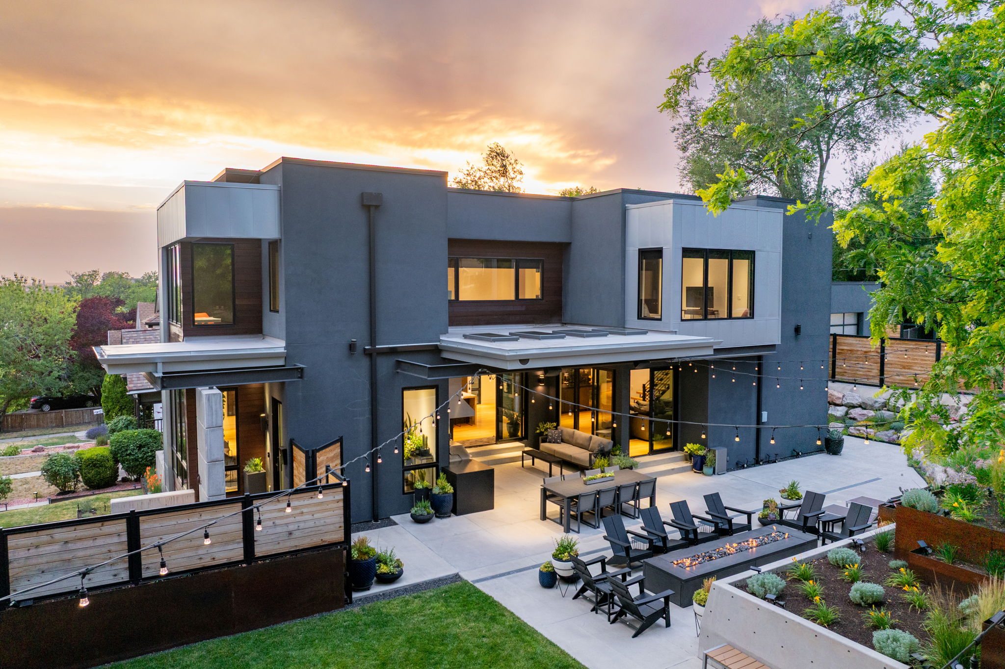 Modern architectural residence featuring a large patio, built-in fire pit, multiple sliding glass doors, and a terraced landscaped garden
