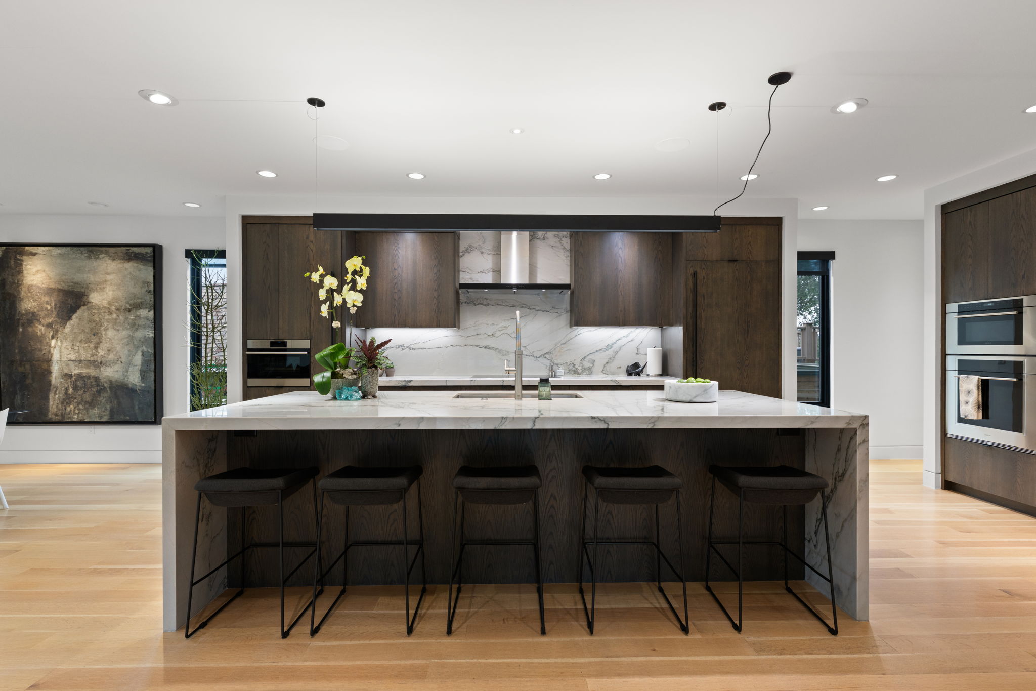 Expansive kitchen featuring a waterfall island with stone countertop, wood-finish cabinetry, stainless steel appliances, and wood-finish flooring