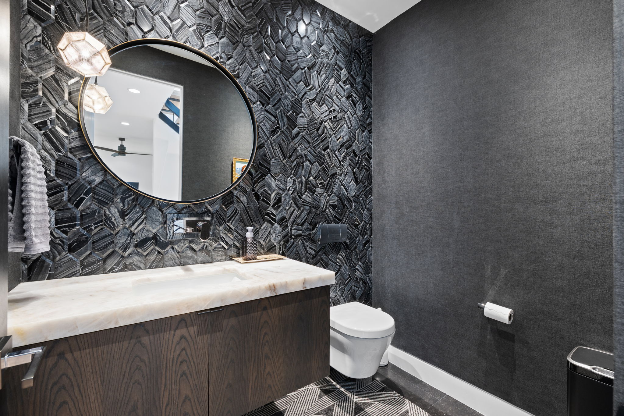 Powder room featuring a stone accent wall with geometric pendant lighting, a round mirror, and a wall-mounted faucet