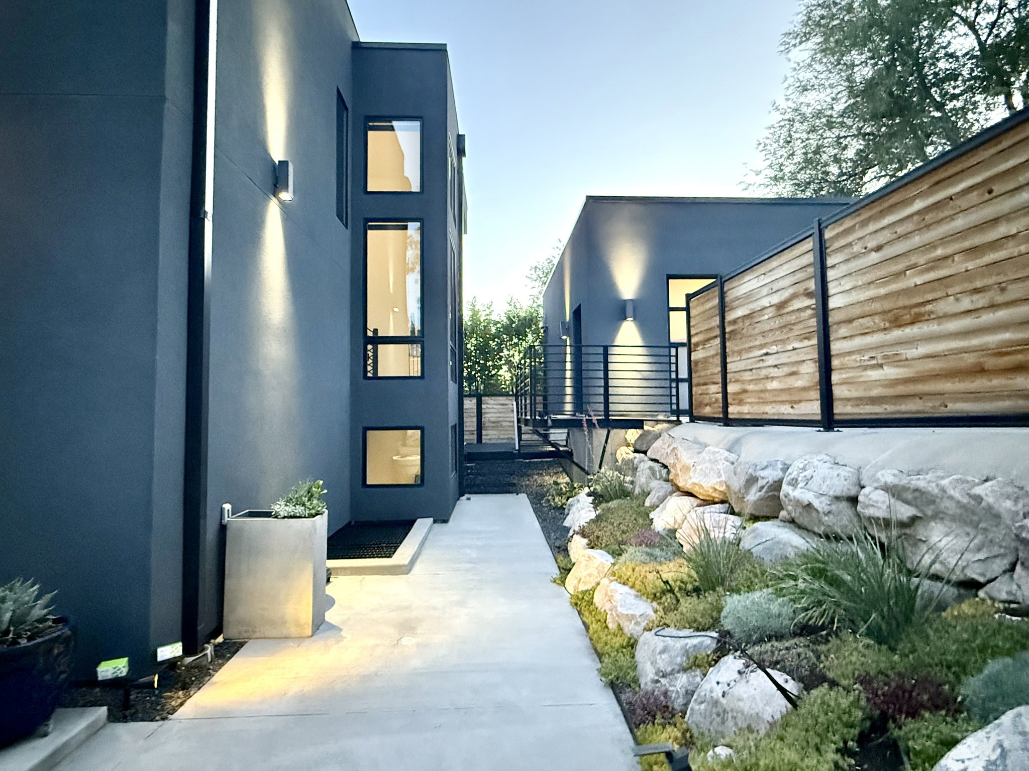 Contemporary exterior architecture featuring dark gray stucco, modern black-framed windows, and sleek outdoor wall sconces