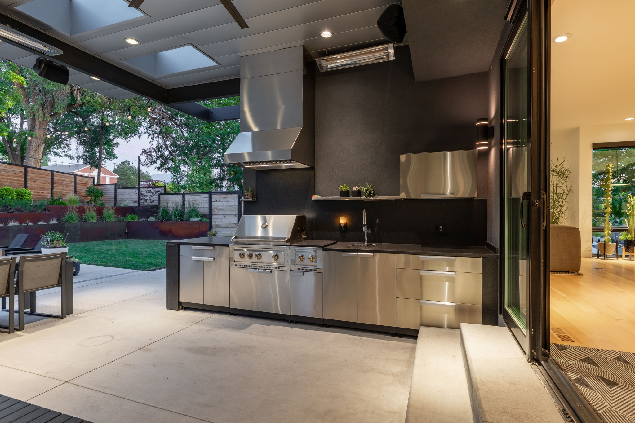Outdoor kitchen featuring stainless steel cabinetry, integrated grill, range hood, and sink with dark countertops