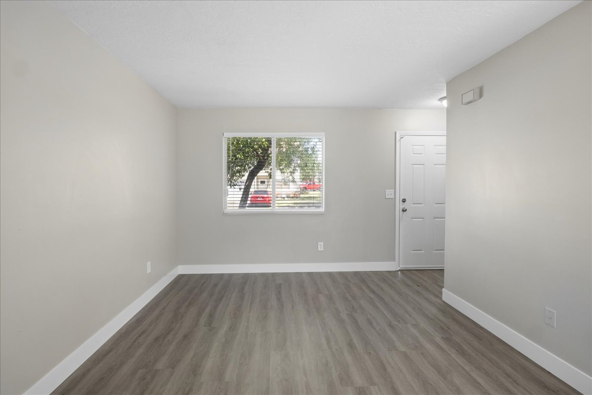Spacious room featuring wood-finish flooring, light gray wall paint, white baseboards, and a window with blinds