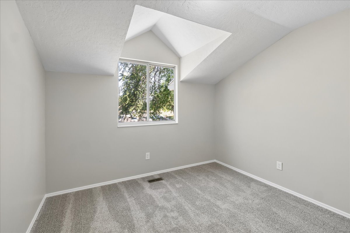 Vaulted ceiling space featuring a large window, light gray walls, and gray carpet flooring
