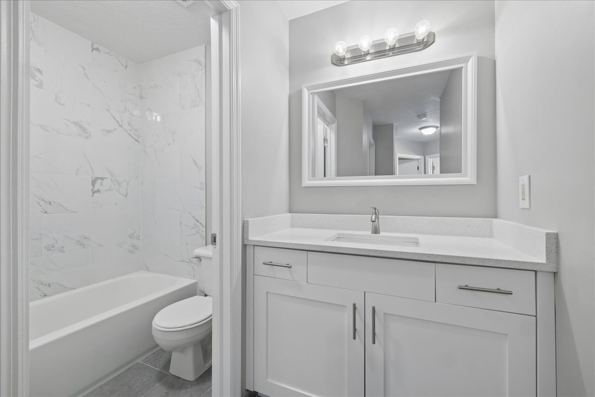 Contemporary bathroom featuring a white vanity with shaker-style cabinetry, a solid surface countertop, and a rectangular undermount sink