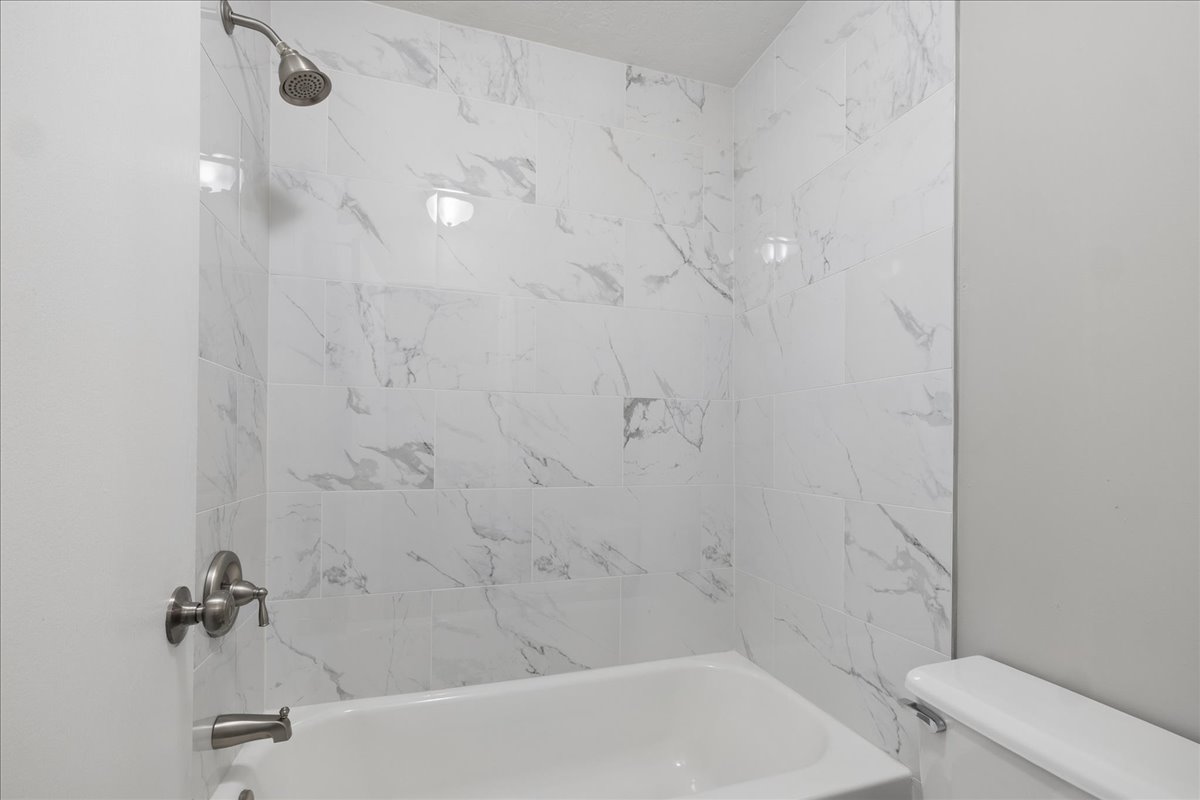 Bathroom featuring a white bathtub, white marble-look tile surround, and brushed nickel fixtures