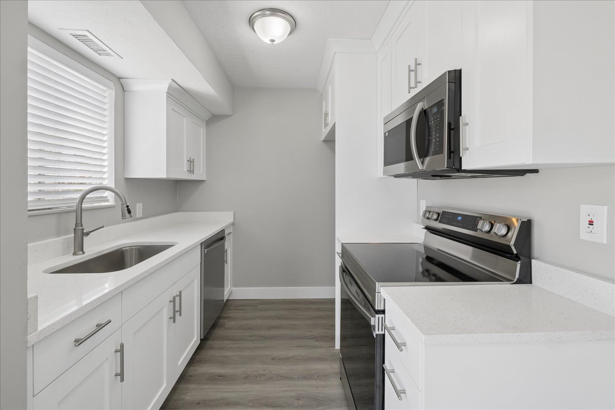 Contemporary kitchen featuring white cabinetry, light countertops, stainless steel appliances, and wood-finish flooring