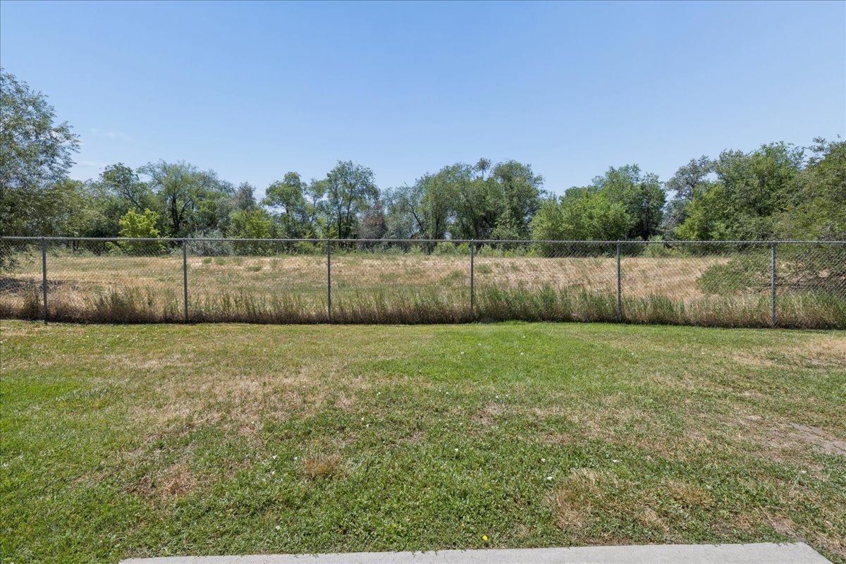 Expansive outdoor space featuring a chain-link fence bordering a grassy area and mature trees