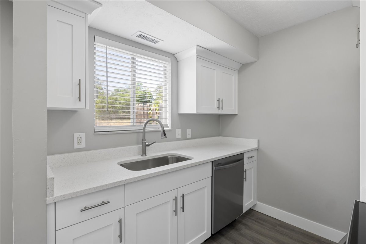 Kitchen area with white shaker cabinetry, light-toned countertops, and a stainless steel sink with a high-arc faucet
