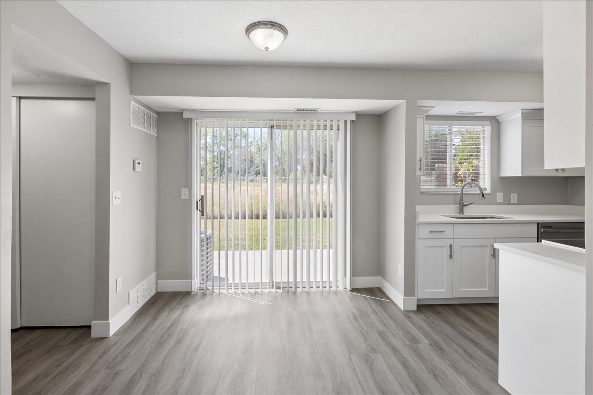Spacious living area featuring wood-finish flooring, sliding glass patio doors with vertical blinds, and a neutral color palette