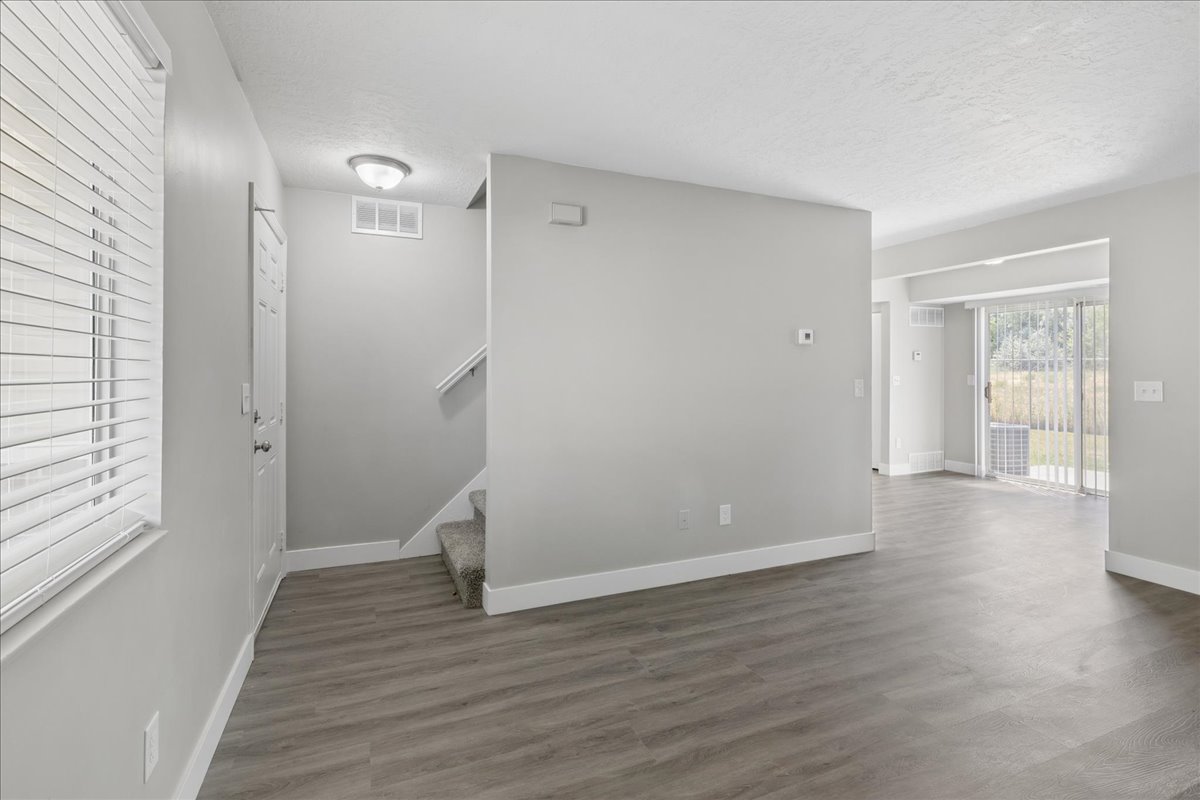 Open-concept living area featuring wood-finish flooring, light grey wall tones, white trim, and a sliding glass door leading to the exterior