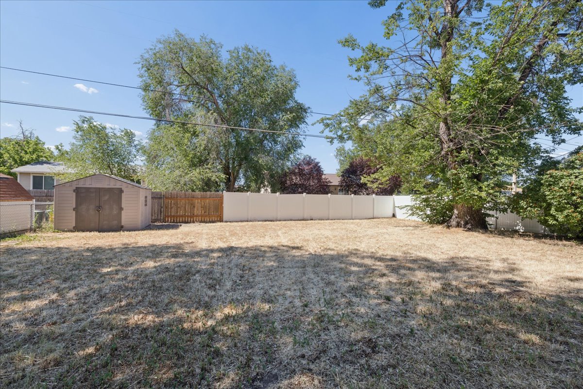 Spacious backyard featuring a storage shed, wood privacy fencing, and mature trees