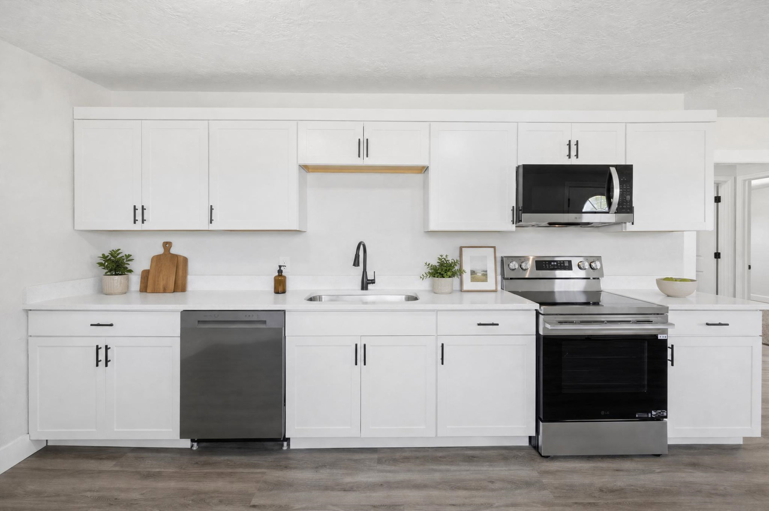 Modern kitchen featuring white cabinetry with matte black hardware, white countertops, and stainless steel appliances including a range, microwave, and dishwasher