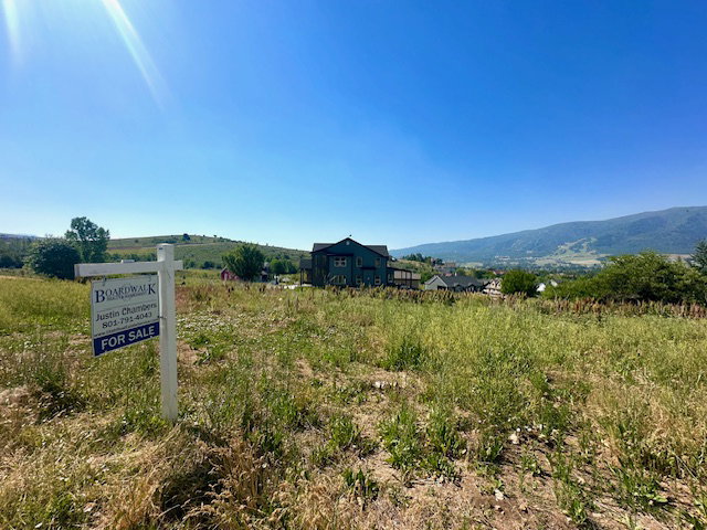 Expansive land parcel featuring natural ground cover, distant mountain ranges, and nearby residential structures