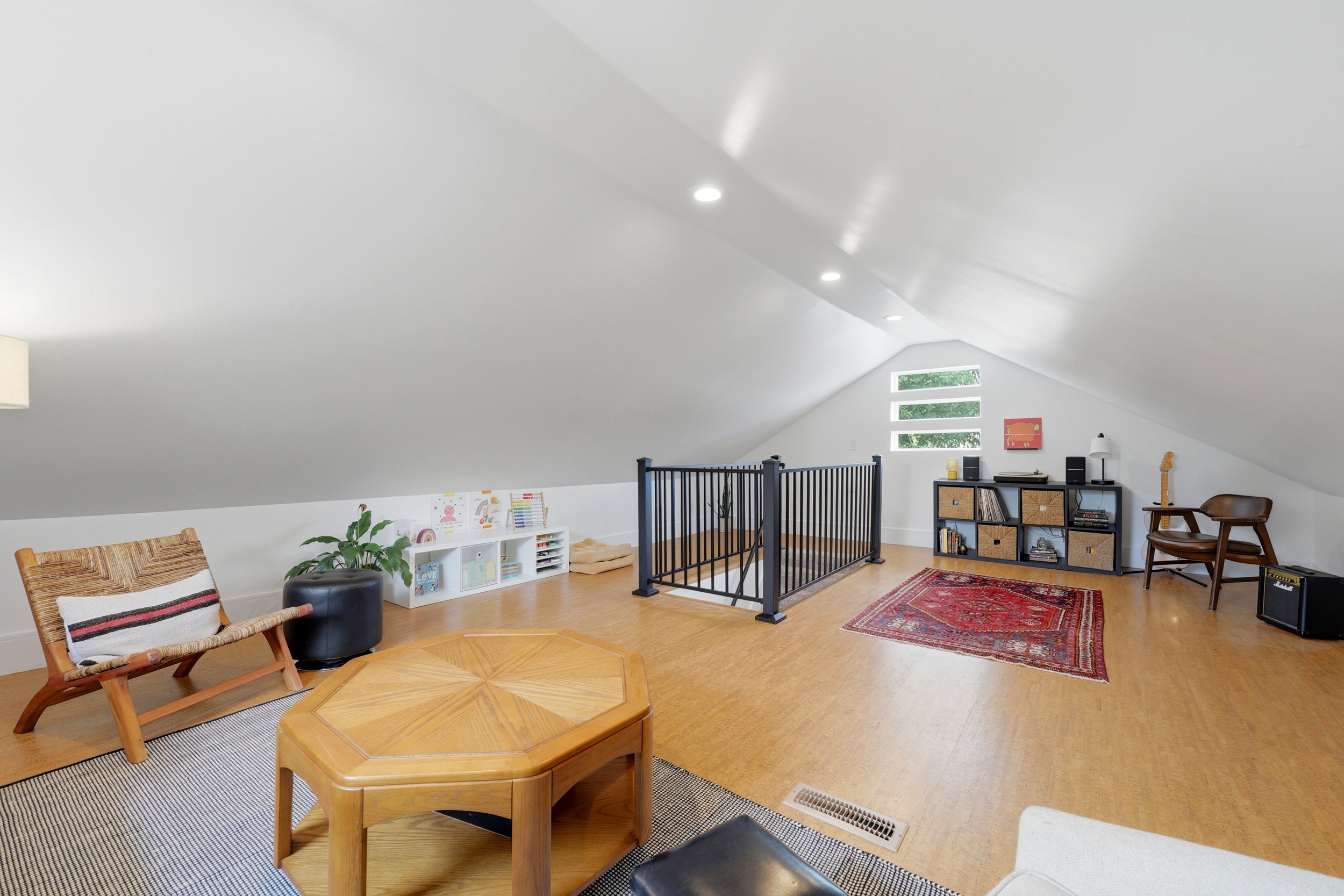Spacious loft area featuring light wood-finish flooring, recessed lighting, and a black metal railing