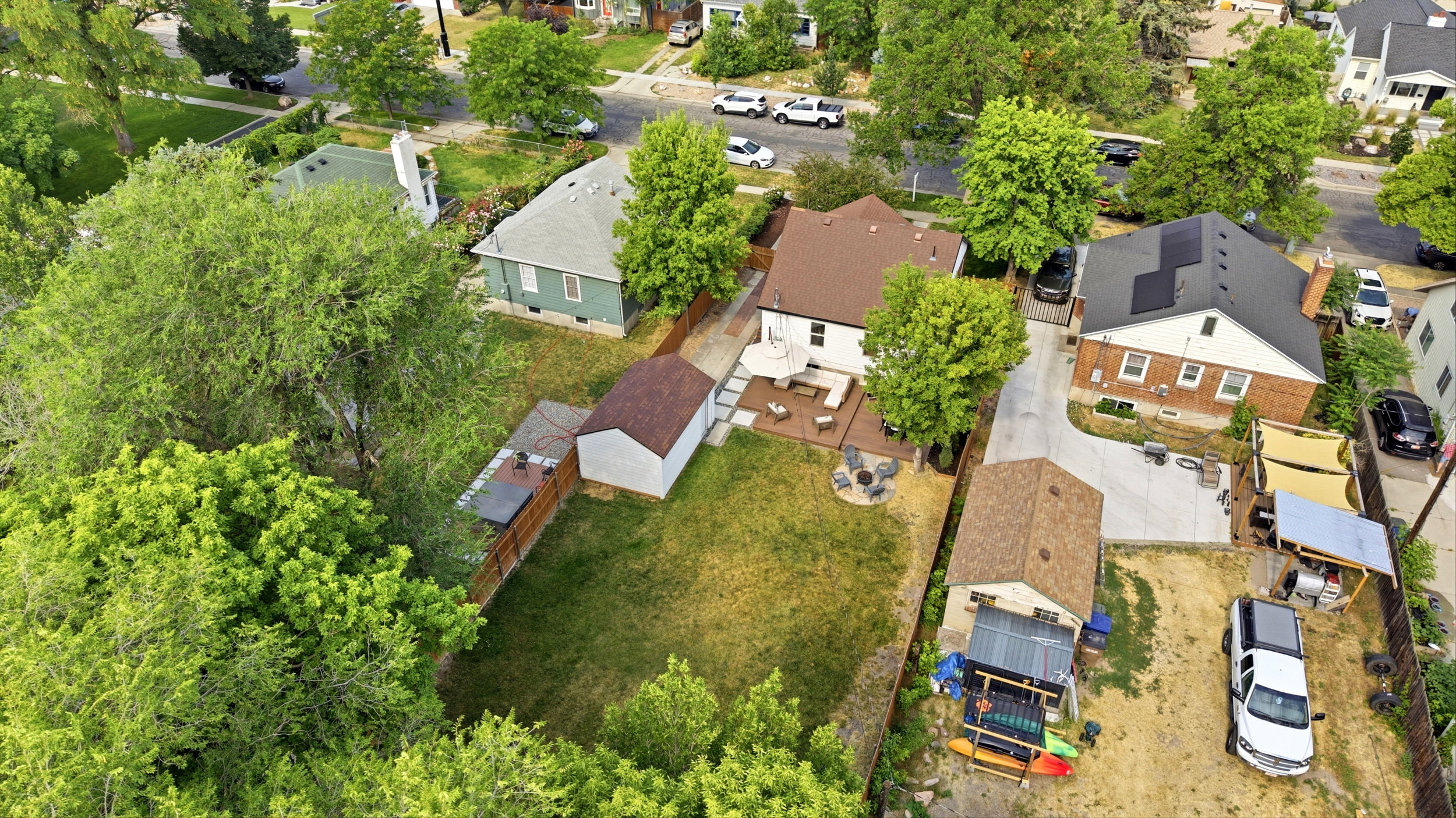 Spacious backyard featuring a manicured lawn, an outdoor deck with seating, a detached storage shed, a privacy fence, and mature trees