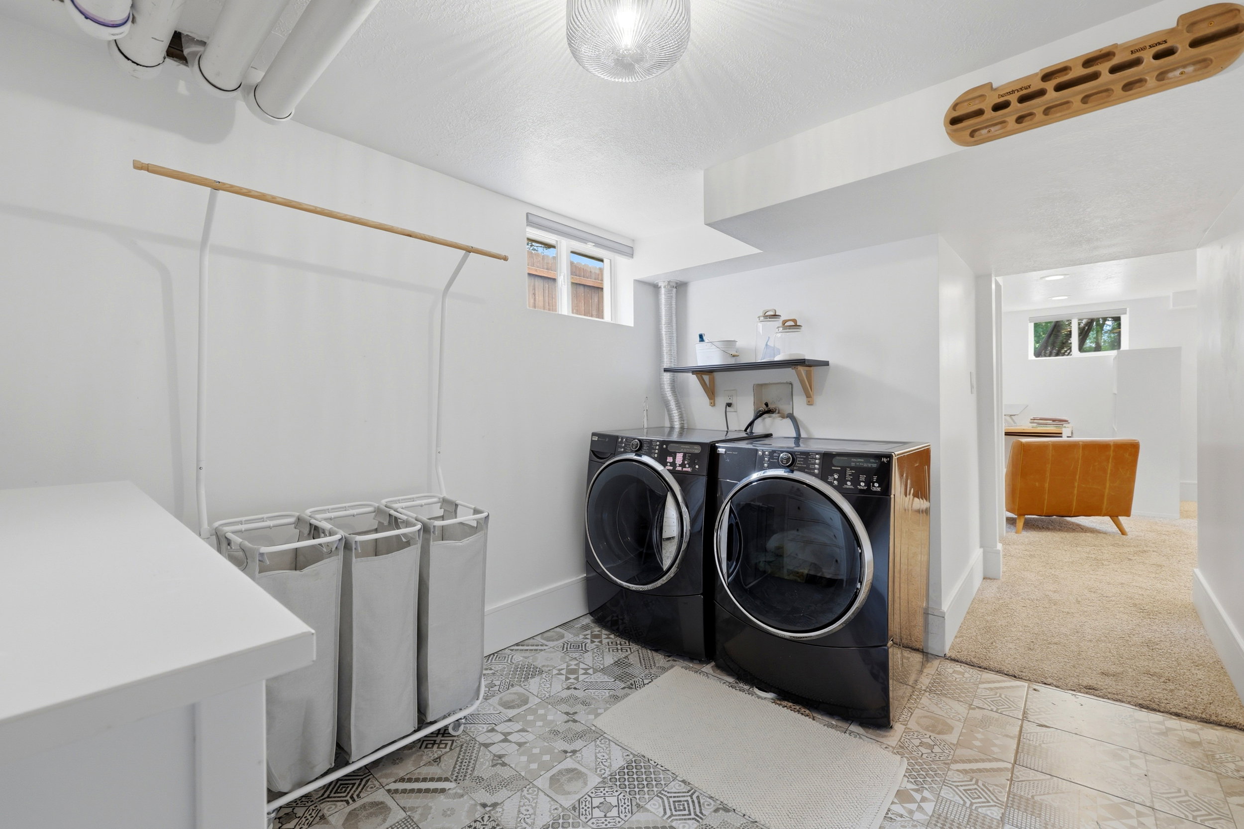 Dedicated laundry area featuring patterned tile flooring, a pair of dark-finish front-load appliances, a built-in shelf, and a ceiling-mounted light fixture