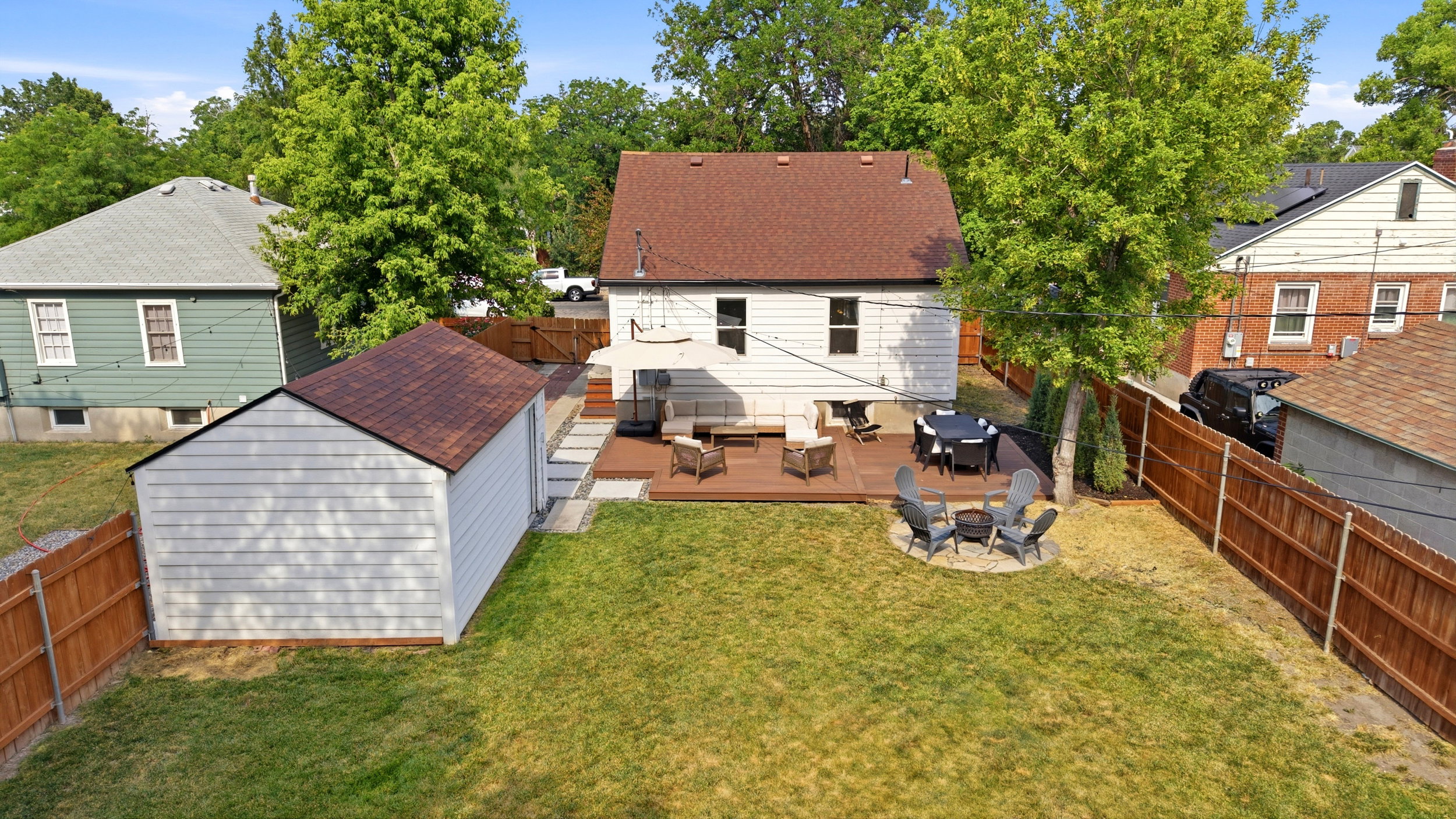 Expansive backyard featuring a multi-level wood deck, a built-in fire pit with stone surround, a manicured lawn, a detached shed with a shingled roof, and a privacy fence