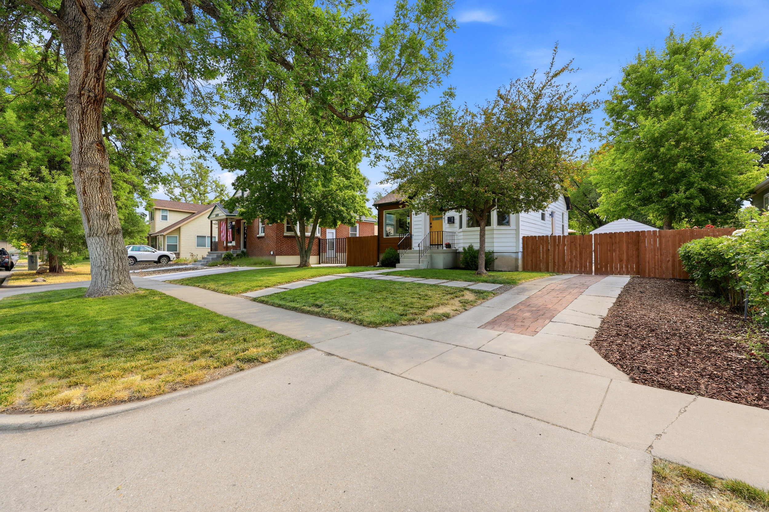 Street view featuring a paved sidewalk, mature trees, and a manicured lawn