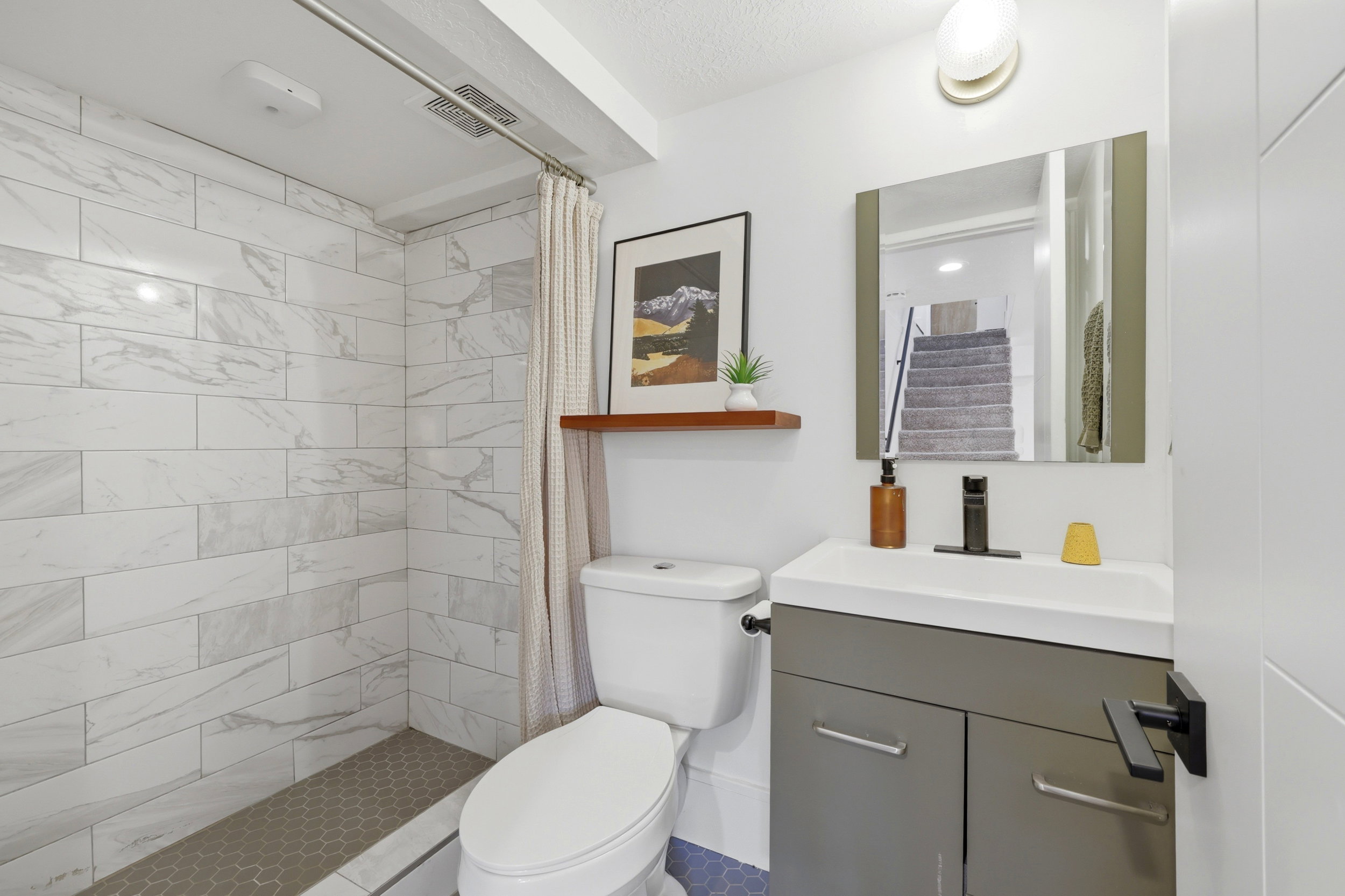 Bathroom featuring a subway-tiled shower with a hexagonal tile floor, a contemporary vanity with a white countertop, a rectangular mirror, and matte black fixtures