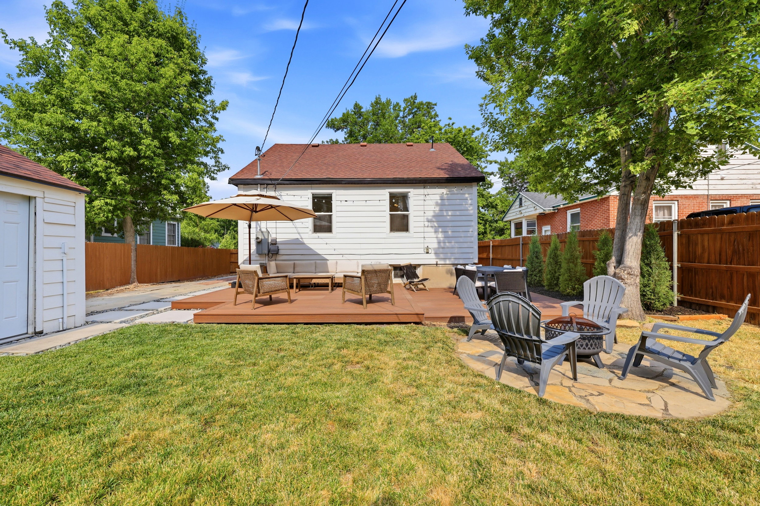 Expansive backyard featuring a manicured lawn, a multi-level wood-finish deck, a natural stone patio, a privacy fence, and mature trees