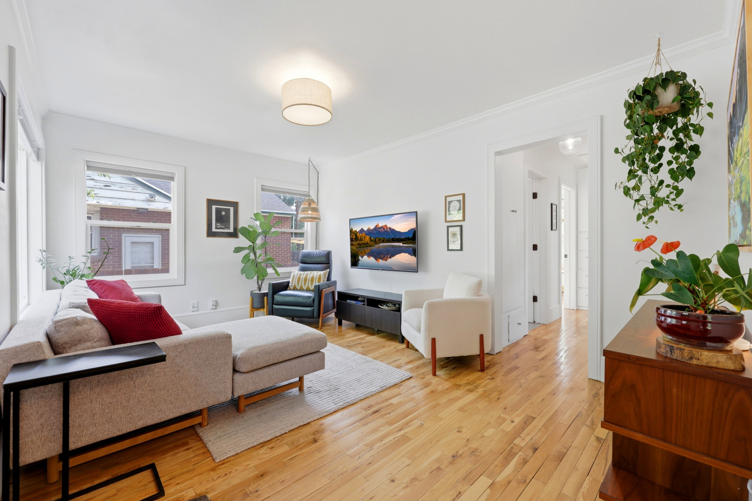 Spacious living area featuring polished wood flooring, multiple windows, recessed ceiling light fixtures, a light-toned area rug, and white wall finishes