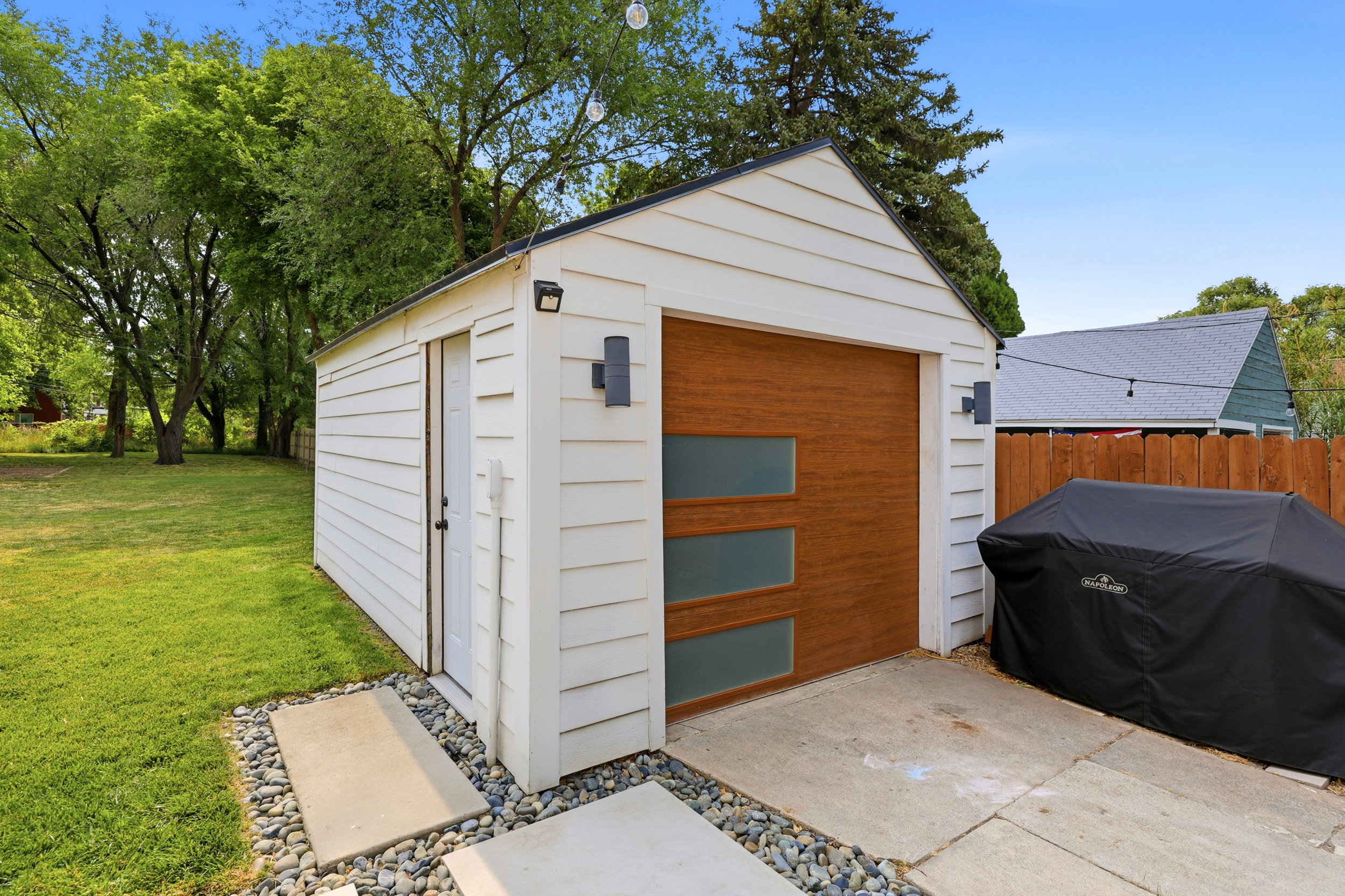 Detached garage featuring a wood-finish garage door with frosted glass panels, white horizontal siding, and modern exterior lighting fixtures