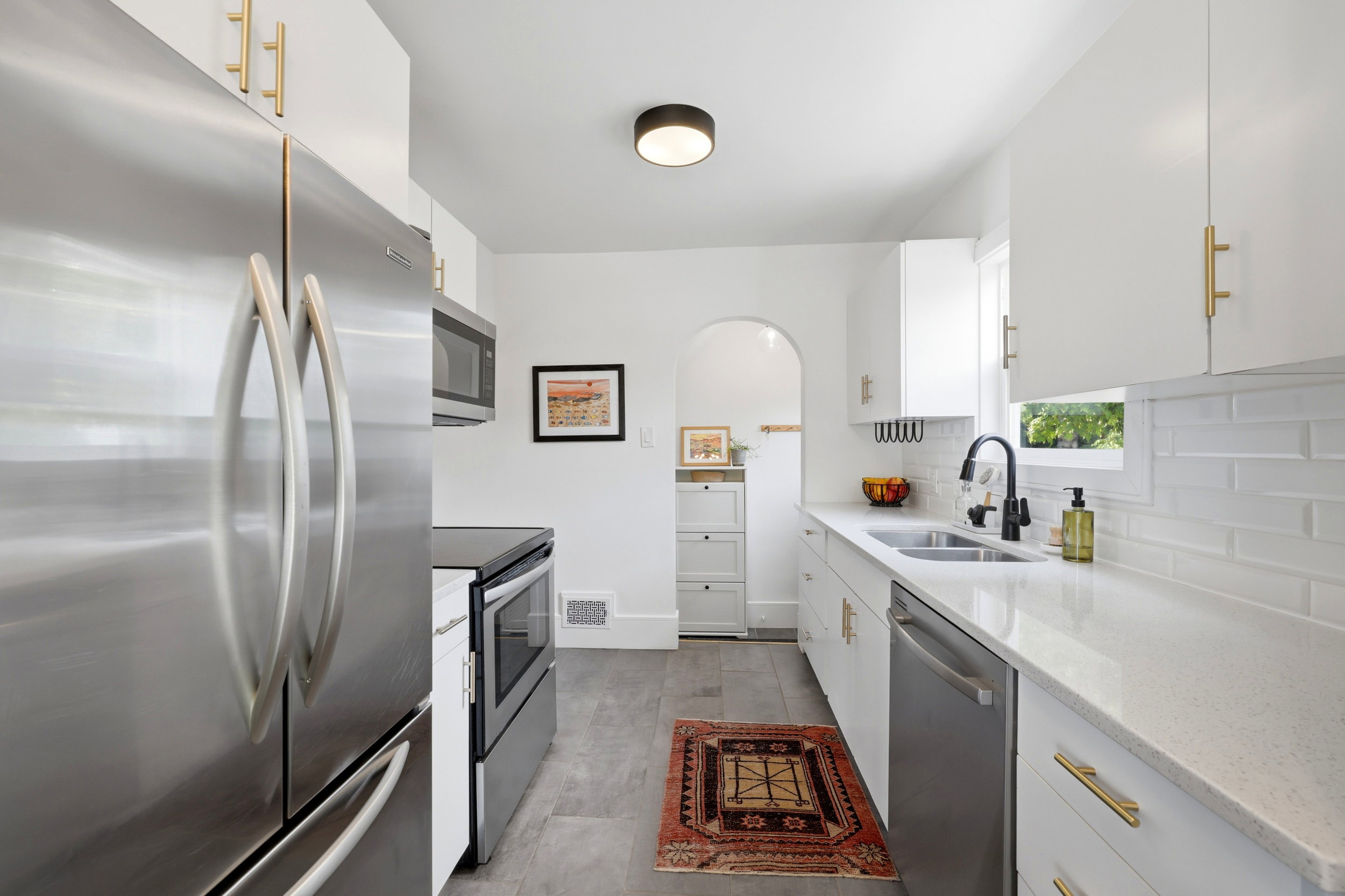 Contemporary kitchen featuring stainless steel appliances, white cabinetry with gold-tone hardware, and light-toned countertops